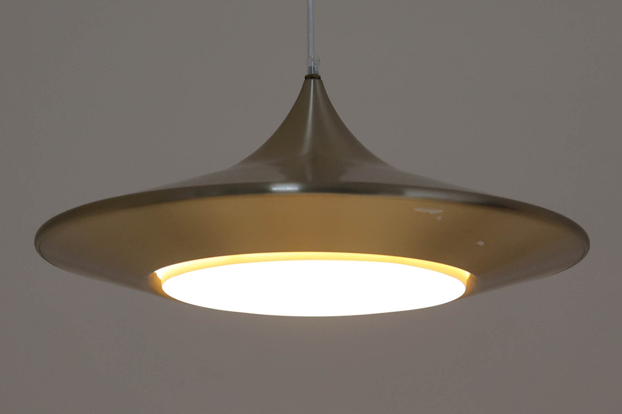 デンマークの照明メーカーLyfa社による、デザイナーEjnar B. mielby（アイナー・B・ミェルビー）が手がけた「Kuli（クーリ）」ペンダントライト。特徴的なホーン型のフォルムと、美しく仕上げられた真鍮カラーのシェードが印象的なビンテージ照明です。直径49cmと存在感のあるサイズ感で、ダイニングテーブルの上などにおすすめです。下面にはグリッド状のルーバーが備わっており、光源を柔らかく拡散しつつ眩しさを軽減する構造となっています。ソケット部分はE26口金、コードは引っ掛けシーリング仕様で、設置も簡単です。経年に伴う小傷や塗装剥がれが一部見られますが、全体としてはビンテージらしい雰囲気を保っています。空間にミッドセンチュリーのエッセンスを加える一品としておすすめです。