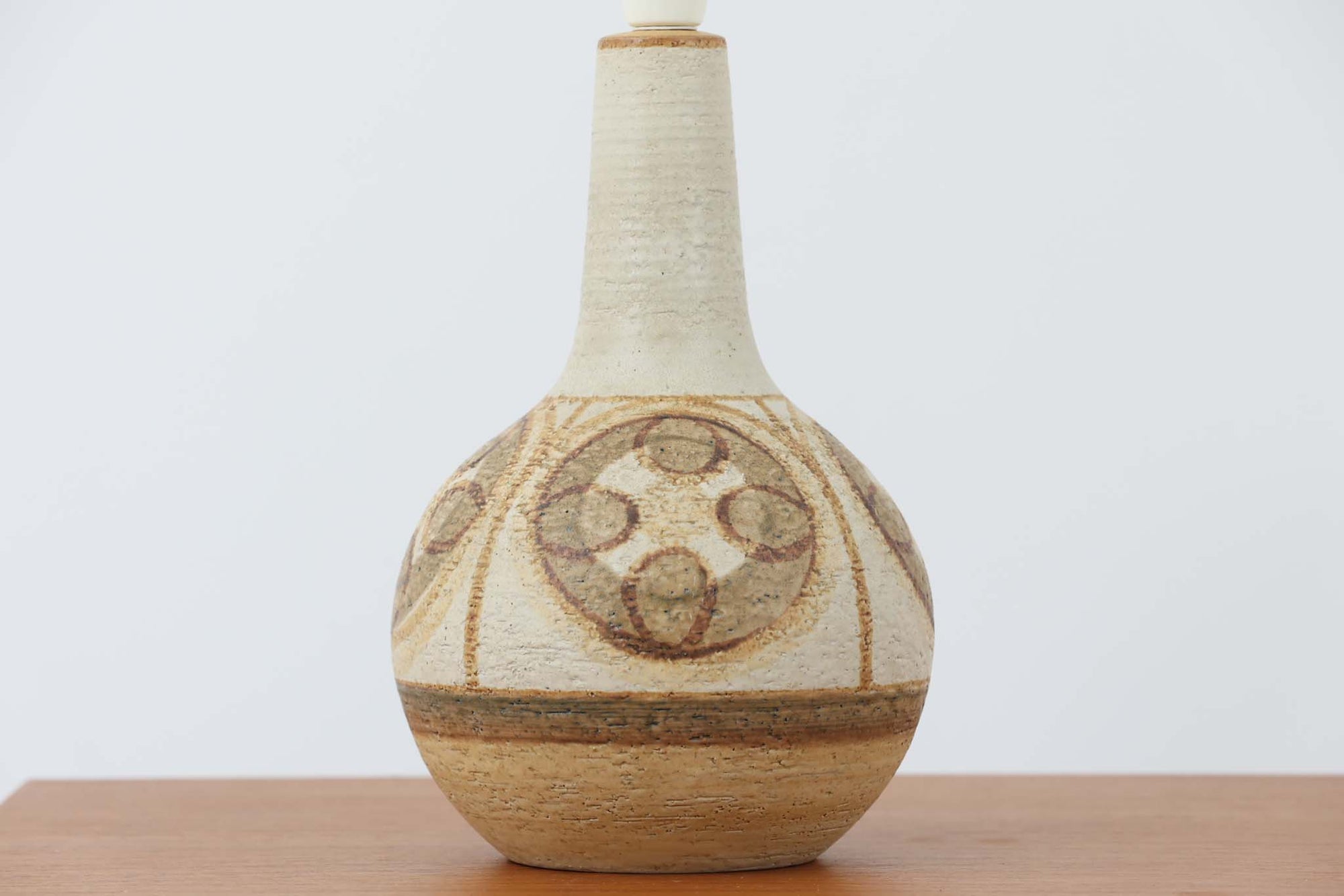 デンマーク・ボーンホルム島の名窯 SOHOLM（スーホルム）によるヴィンテージのテーブルランプです。ふっくらとしたボディに施された幾何学模様が印象的で、素朴であたたかみのある釉薬の風合いが魅力。北欧らしいナチュラルな空気感を空間に添えてくれます。高さは約48cmとやや大きめで、しっかりとした存在感がありながらも落ち着いた佇まいです。シェードは新品のリネン製に交換済み。やさしい光がファブリック越しにふんわりと広がり、ベッドサイドやリビングのアクセントにぴったりです。北欧陶器ならではの土の質感と落ち着いた色彩をお楽しみください。