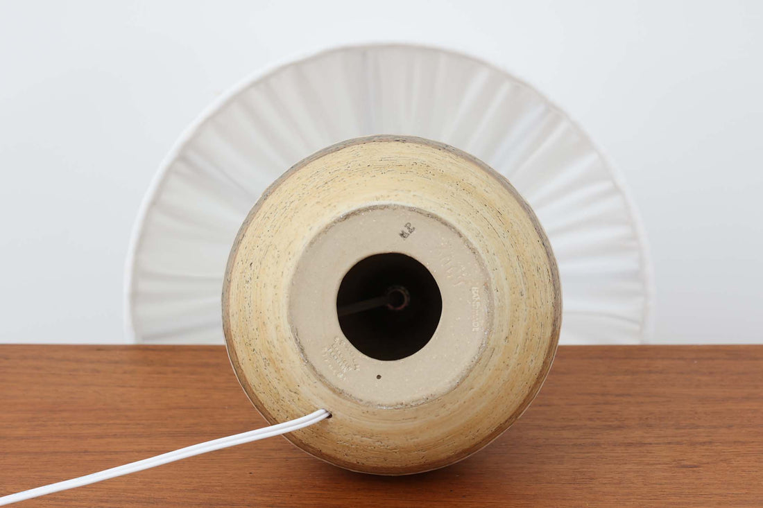 デンマーク・ボーンホルム島の名窯 Soholm（スーホルム）によるヴィンテージのテーブルランプです。ふっくらとしたボディに施された幾何学模様が印象的で、素朴であたたかみのある釉薬の風合いが魅力。北欧らしいナチュラルな空気感を空間に添えてくれます。高さは約48cmとやや大きめで、しっかりとした存在感がありながらも落ち着いた佇まいです。シェードは新品のリネン製に交換済み。やさしい光がファブリック越しにふんわりと広がり、ベッドサイドやリビングのアクセントにぴったりです。北欧陶器ならではの土の質感と落ち着いた色彩をお楽しみください。