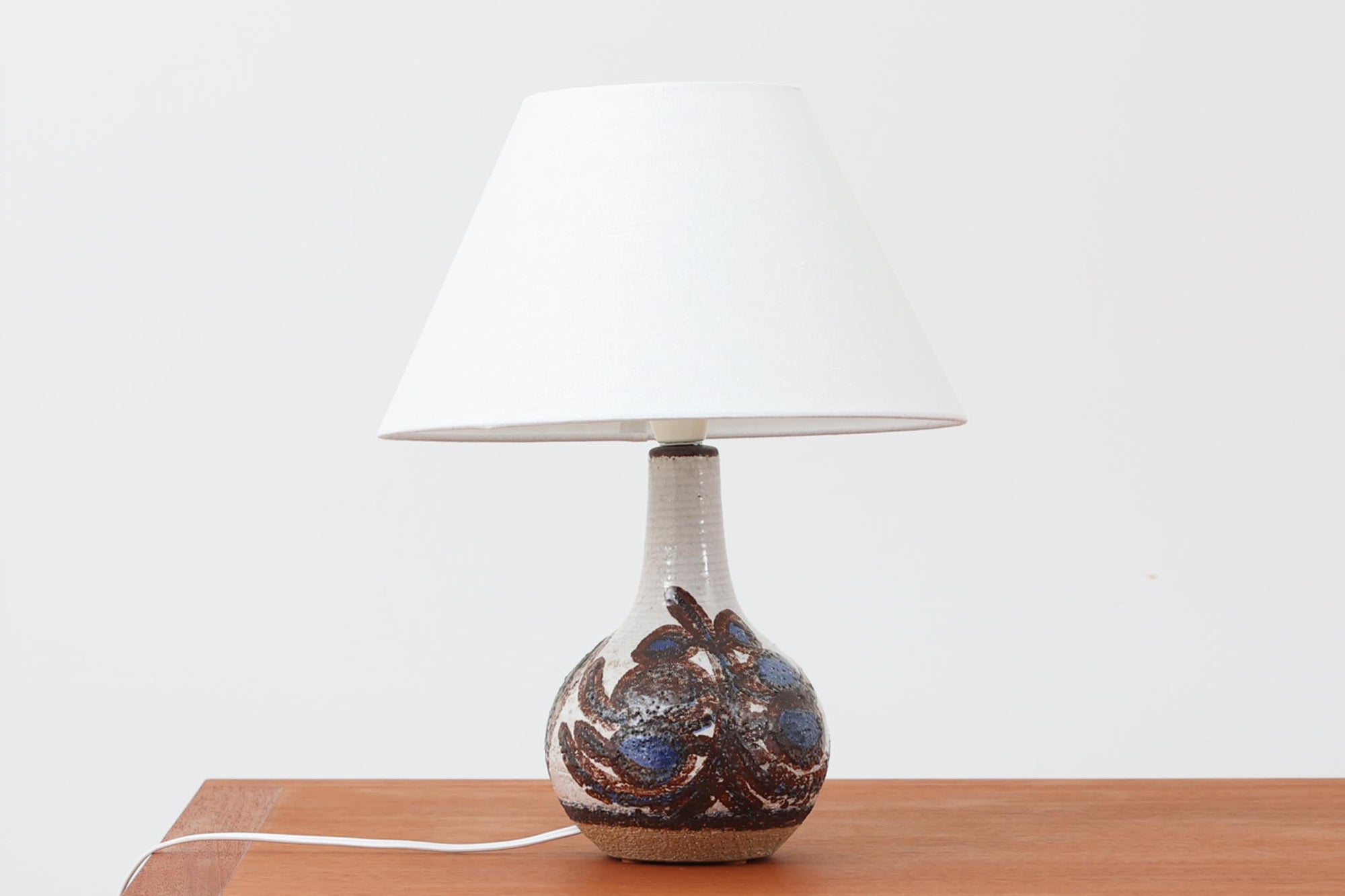 デンマーク・ボーンホルム島の陶器メーカーSOHOLM（スーホルム）によるヴィンテージテーブルランプ。手仕事の温もりを感じる有機的なフォルムに、抽象的で力強い絵柄が施されています。グリーンとブルーのアクセントが印象的で、陶肌の素朴な質感とも美しく調和しています。シェードは新品のリネン製。北欧らしい落ち着いた存在感があり、空間にやさしい灯りと彩りを添えてくれます。