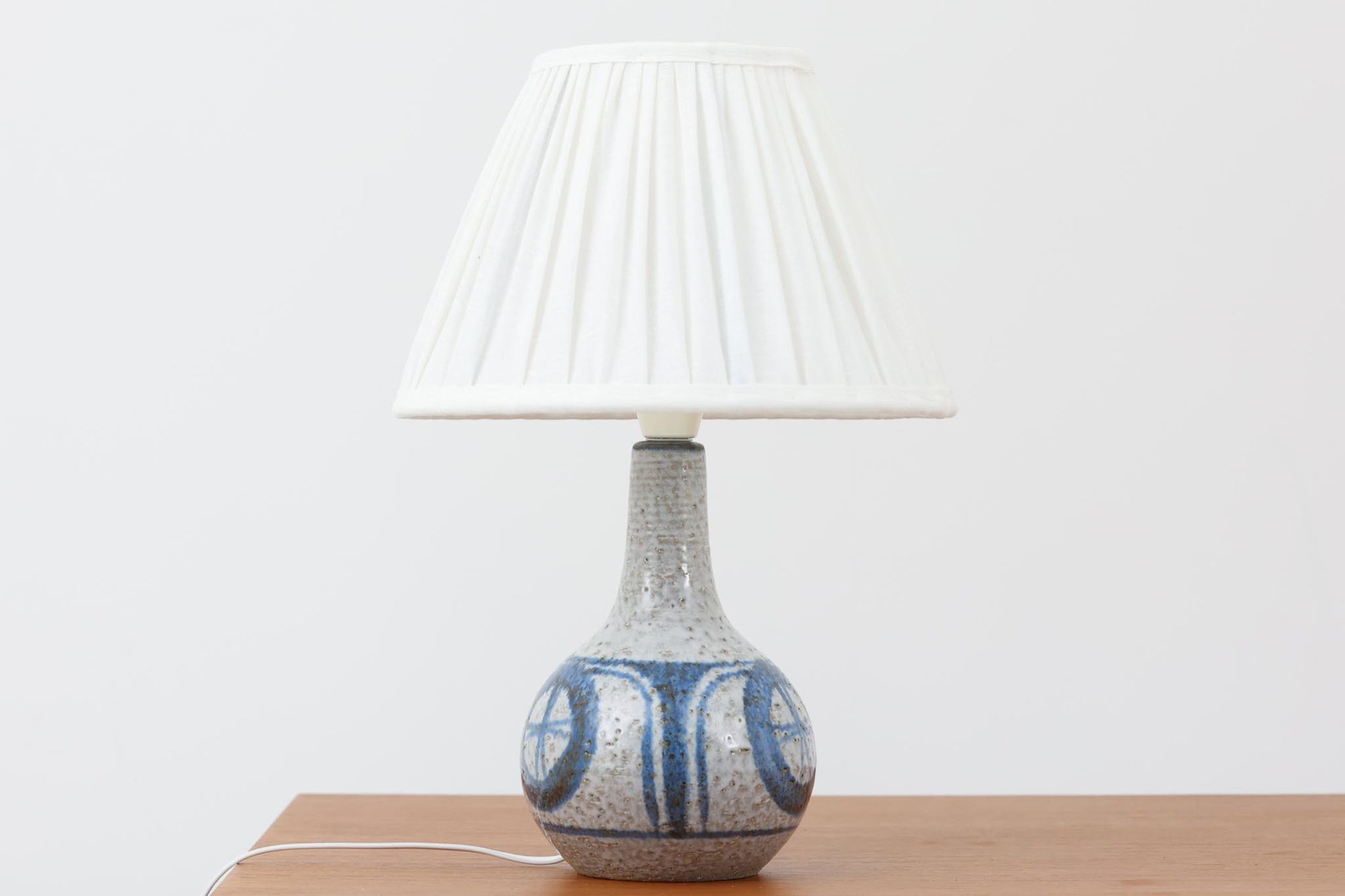 デンマーク・ボーンホルム島の陶器メーカーSOHOLMによるヴィンテージテーブルランプ。ざらりとした質感のある陶器ボディに、藍色を基調とした幾何学模様が手描きされています。丸みのあるフォルムが愛らしく、落ち着いた色合いは空間に優しく馴染みます。シェードは新品のリネン製に交換済みです。