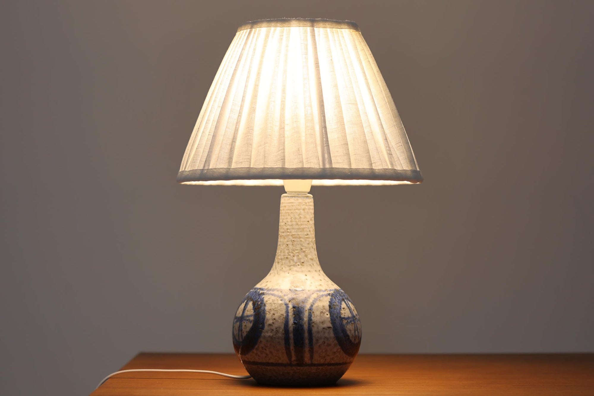 デンマーク・ボーンホルム島の陶器メーカーSOHOLMによるヴィンテージテーブルランプ。ざらりとした質感のある陶器ボディに、藍色を基調とした幾何学模様が手描きされています。丸みのあるフォルムが愛らしく、落ち着いた色合いは空間に優しく馴染みます。シェードは新品のリネン製に交換済みです。