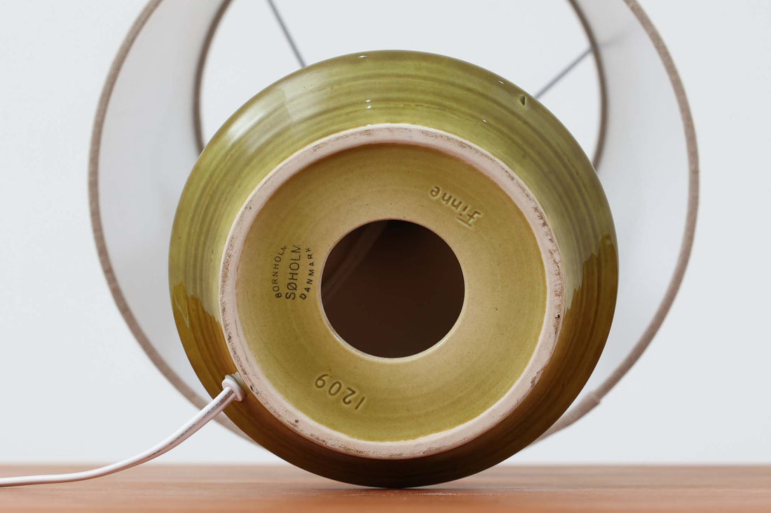 デンマーク・ボーンホルム島の陶器工房Soholmによるテーブルランプ。陶肌に浮かび上がる幾何学模様が印象的で、まるで目のようなユニークな装飾が施されています。艶のあるグリーンの釉薬が奥行きを感じさせ、どこか神秘的な雰囲気を漂わせます。シェードは新品のリネン製で、ベースとの相性も良く、空間に柔らかな光を添えてくれます。底面には「Soholm DENmARK」のサインが確認できます。北欧ヴィンテージならではの存在感ある一点物です。