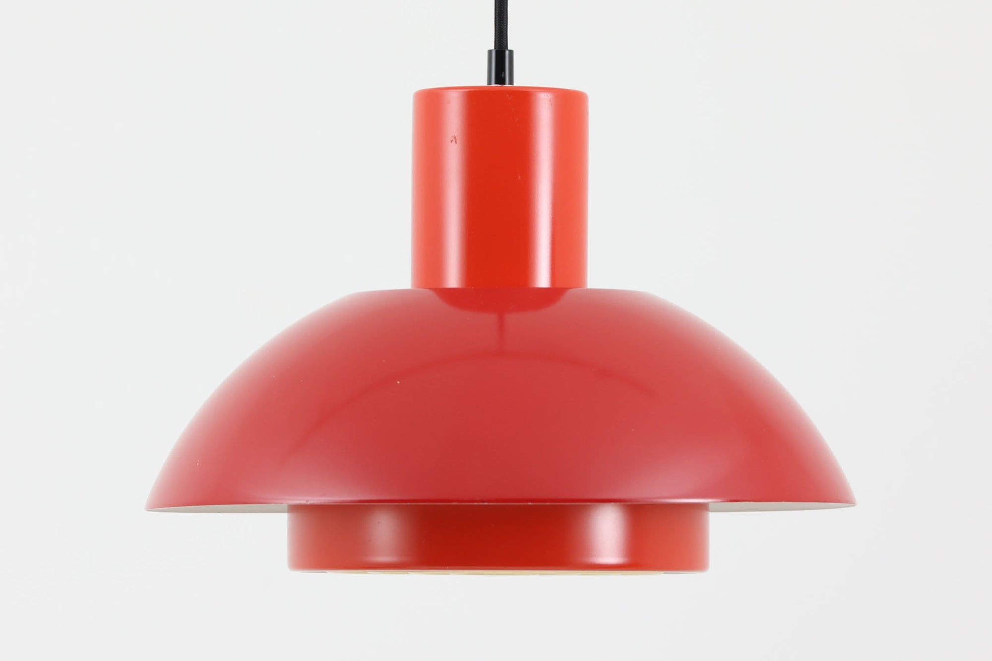 Fog & Morup（フォグ＆モーラップ）社より、Jo Hammerborg（ヨー・ハーマボー）によってデザインされた「Lakaj」ペンダントライトです。直径34cmのシェードは、赤の外装と内側のホワイト＆ボトムカバーの淡いイエローの配色が美しい光を柔らかく拡散し、空間に温もりと視覚的なアクセントを与えます。点灯時にはシェード上部から漏れる光が間接照明としても機能し、北欧ビンテージ家具と調和する洗練された雰囲気を演出します。ダイニングやリビングの照明に最適な、希少性と機能美を兼ね備えた一灯です。