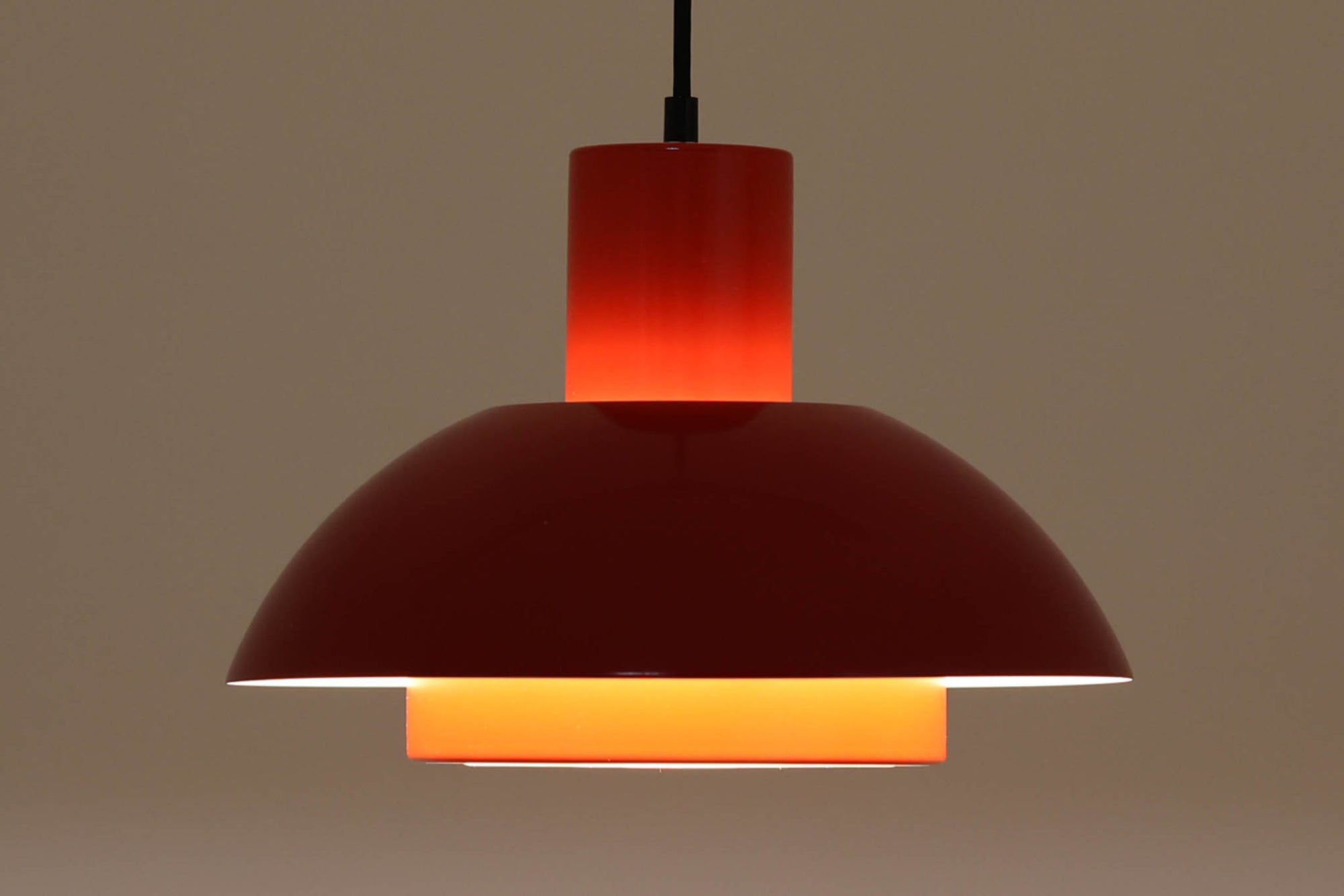 Fog & Morup（フォグ＆モーラップ）社より、Jo Hammerborg（ヨー・ハーマボー）によってデザインされた「Lakaj」ペンダントライトです。直径34cmのシェードは、赤の外装と内側のホワイト＆ボトムカバーの淡いイエローの配色が美しい光を柔らかく拡散し、空間に温もりと視覚的なアクセントを与えます。点灯時にはシェード上部から漏れる光が間接照明としても機能し、北欧ビンテージ家具と調和する洗練された雰囲気を演出します。ダイニングやリビングの照明に最適な、希少性と機能美を兼ね備えた一灯です。