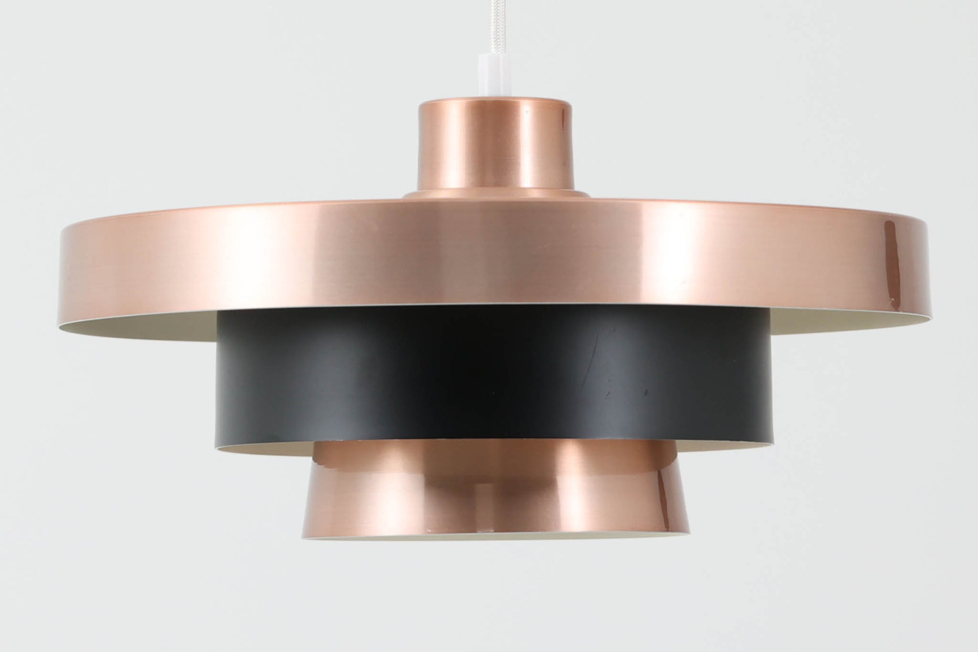 北欧より買い付けたビンテージのペンダントライトです。光をやさしく拡散するルーバー構造のシェードデザインが特徴で、点灯時には内側の光が美しく反射し、空間に落ち着きのある雰囲気を演出します。外側は艶やかな銅色、内側はホワイトで塗装されており、中央部分にはマットなブラックカラーがアクセントとして配置されています。丸みのあるフォルムと相まって、モダンで洗練された印象を与える一品です。本体サイズは直径34×高さ18cmで、ダイニングやリビングなど幅広い空間にフィットします。メーカーやデザイナーの特定には至っていませんが、北欧らしい優れた造形美と実用性を兼ね備えたアイテムです。