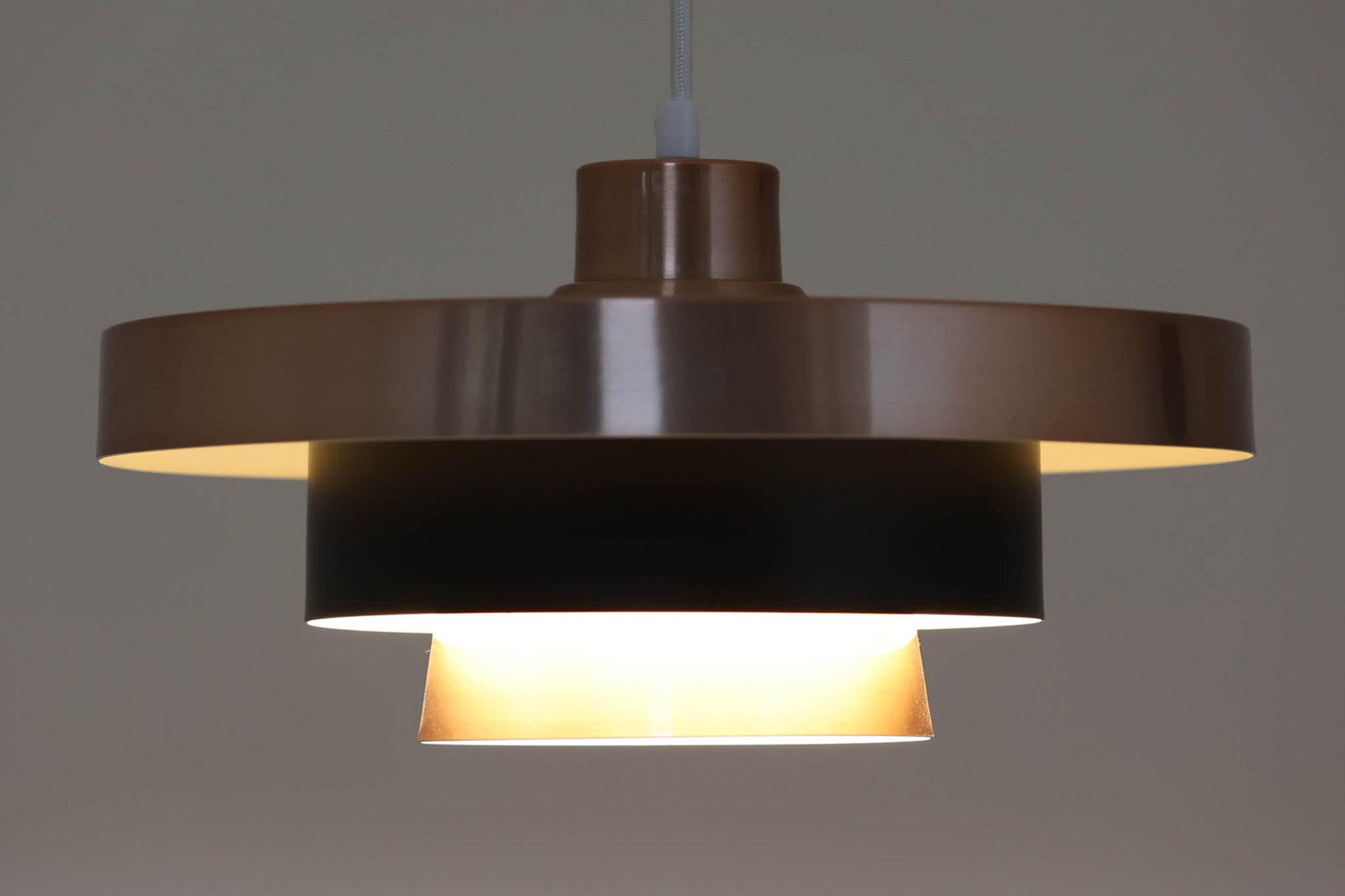 北欧より買い付けたビンテージのペンダントライトです。光をやさしく拡散するルーバー構造のシェードデザインが特徴で、点灯時には内側の光が美しく反射し、空間に落ち着きのある雰囲気を演出します。外側は艶やかな銅色、内側はホワイトで塗装されており、中央部分にはマットなブラックカラーがアクセントとして配置されています。丸みのあるフォルムと相まって、モダンで洗練された印象を与える一品です。本体サイズは直径34×高さ18cmで、ダイニングやリビングなど幅広い空間にフィットします。メーカーやデザイナーの特定には至っていませんが、北欧らしい優れた造形美と実用性を兼ね備えたアイテムです。