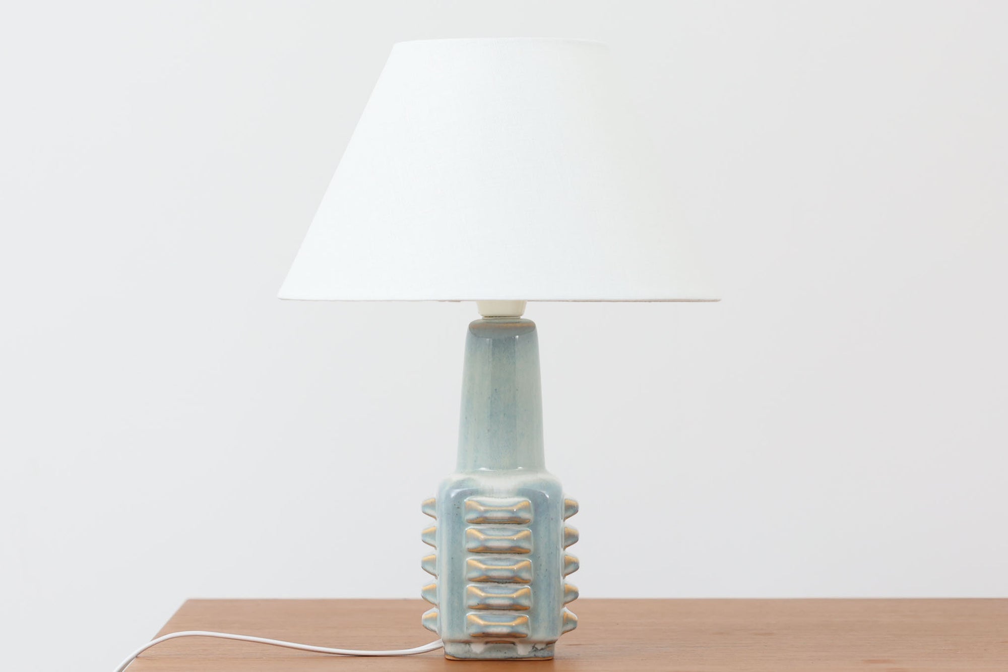 デンマーク・ボーンホルム島の陶器メーカーSOHOLM（スーホルム）で製作されたテーブルランプ。デザイナーはEinar Johansen（アイナー・ヨハンセン）。立体的なレリーフ模様と、ブルーグレーに淡くアイスブルーが重なる美しい釉薬の表情が特徴です。ユニークなフォルムも印象的で、置くだけで空間に存在感をもたらします。シェードは新品のリネン製を合わせています。北欧ヴィンテージらしい温もりと洗練を兼ね備えた一点です。