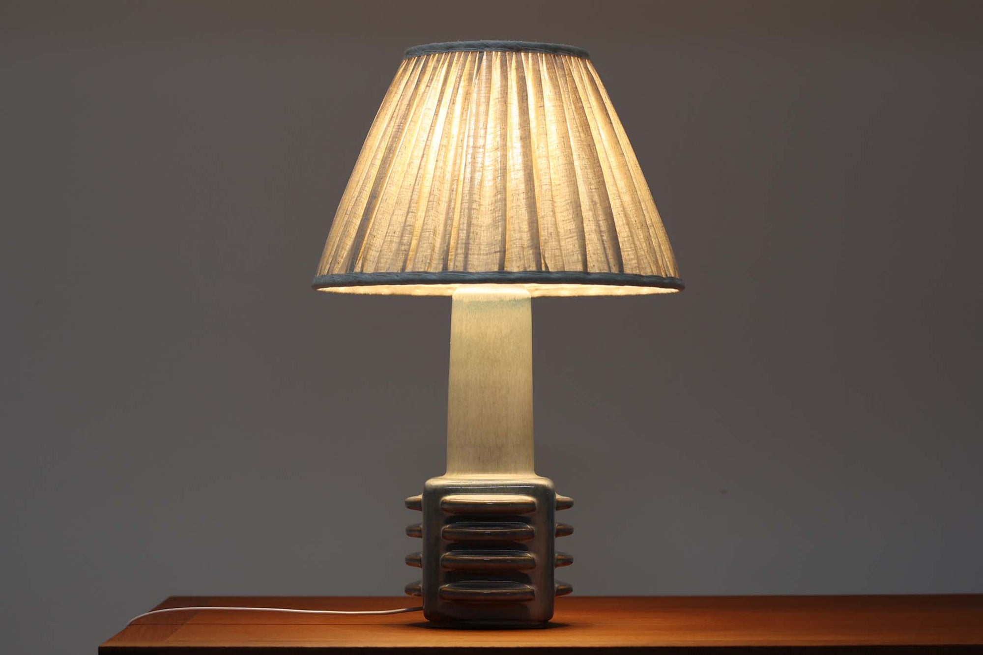 デンマーク・ボーンホルム島の陶器メーカー SOHOLM（スーホルム）で製作されたテーブルランプ。デザイナーは Einar Johansen（アイナー・ヨハンセン）。立体的なレリーフ模様と、ブルーグレーに淡くアイスブルーが重なる美しい釉薬の表情が特徴です。ユニークなフォルムも印象的で、置くだけで空間に存在感をもたらします。高さは約51cmとやや大きめで、サイドボードやコンソールの上などに置くと程よいボリューム感が生まれます。シェードは新品のリネン製を合わせています。北欧ヴィンテージらしい温もりと洗練を兼ね備えた一点です。