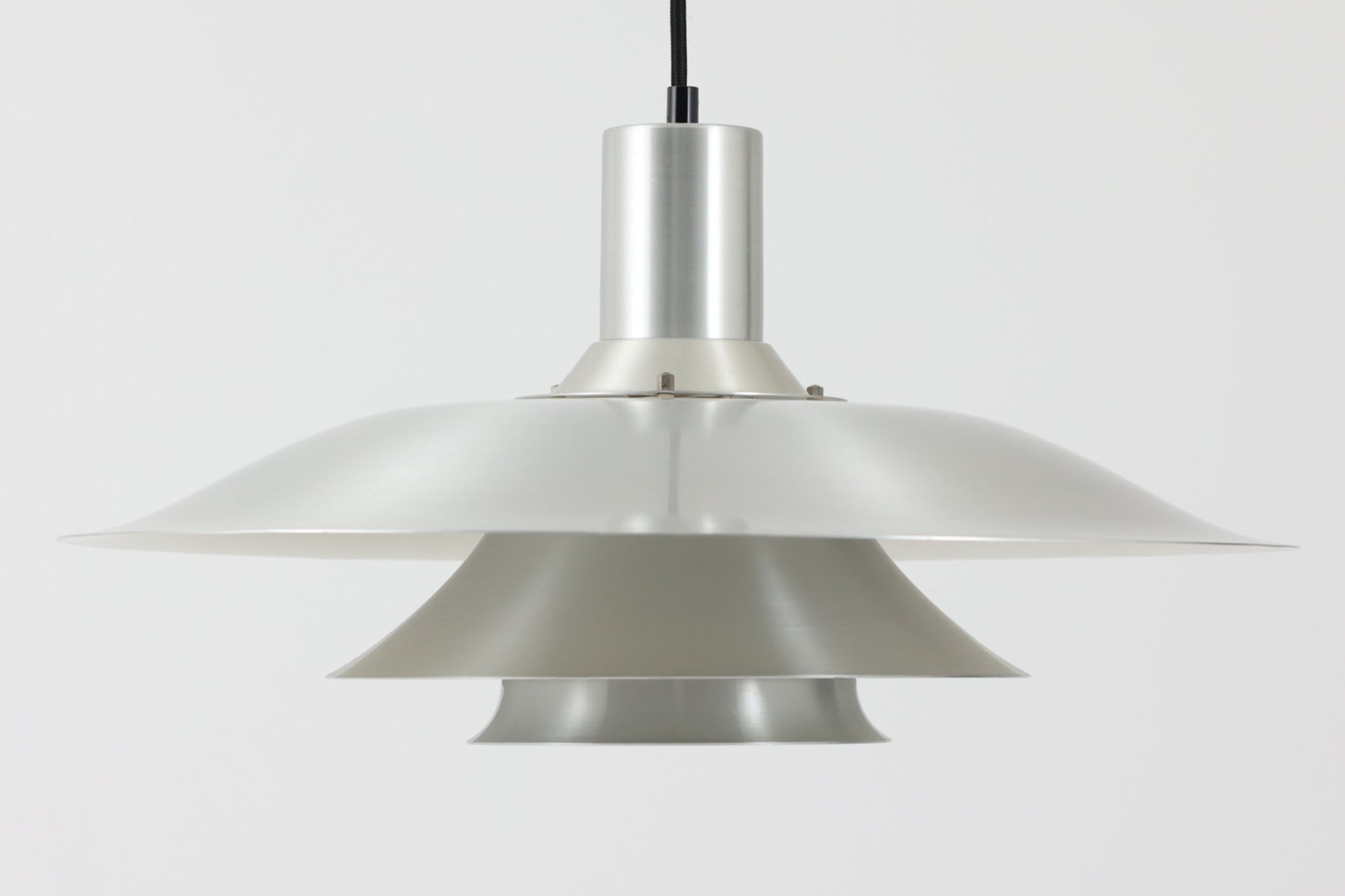 北欧より買い付けたビンテージのペンダントライトです。波打つように重なるルーバーシェードが美しい陰影を生み出し、点灯時には眩しさを抑えながらやわらかな光を広げてくれます。素材はアルミニウムで、全体はシルバートーンで統一され、シャープで洗練された印象を与えるデザインです。直径50×高さ25cmの存在感あるサイズで、ダイニングやリビングの主照明としてもおすすめです。メーカーやデザイナーは不明ですが、北欧らしい合理性と美しさを兼ね備えた一品です。