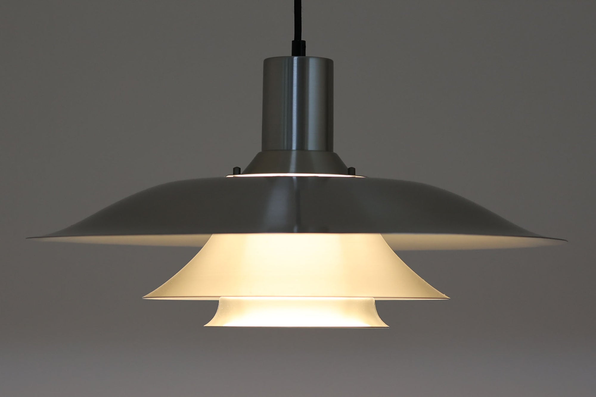 北欧より買い付けたビンテージのペンダントライトです。波打つように重なるルーバーシェードが美しい陰影を生み出し、点灯時には眩しさを抑えながらやわらかな光を広げてくれます。素材はアルミニウムで、全体はシルバートーンで統一され、シャープで洗練された印象を与えるデザインです。直径50×高さ25cmの存在感あるサイズで、ダイニングやリビングの主照明としてもおすすめです。メーカーやデザイナーは不明ですが、北欧らしい合理性と美しさを兼ね備えた一品です。