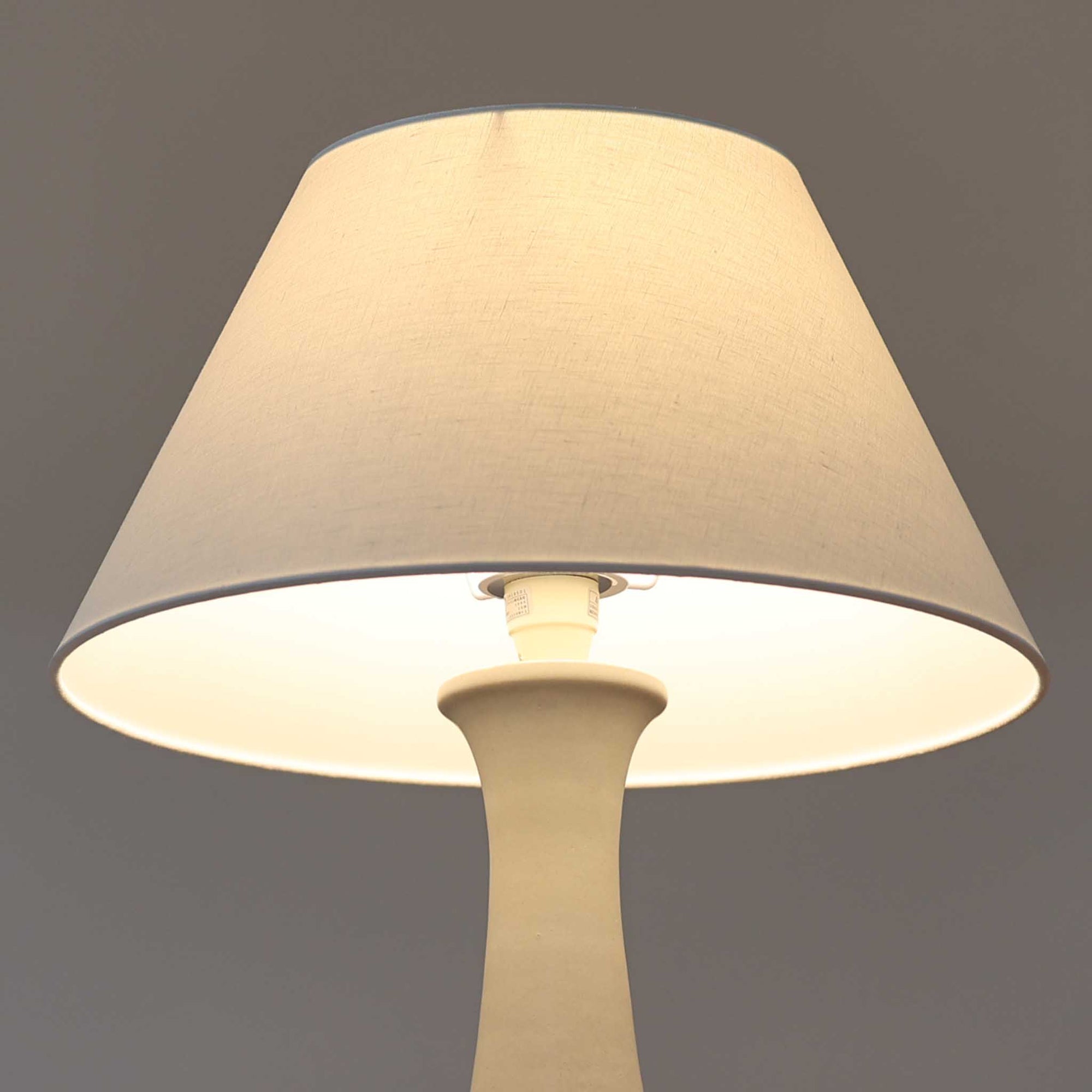 デンマークの照明ブランド Le Klint（レ・クリント）によるテーブルランプで、デザイナーは Ole Boggild（オーレ・ボギル）です。シェードは Le Klint 社製ではありませんが、新品のリネン製プリーツシェードを合わせており、全体として上品で柔らかな印象に仕上がっています。丸みを帯びた陶磁器ベースに、すらりと伸びるネックの造形が美しく、北欧デザインらしい穏やかな佇まいを感じさせます。ややグレーがかったマットな質感が上品で、リネンシェードを通した柔らかな光が空間を優しく包み込みます。シンプルながら存在感があり、リビングやベッドサイドなどさまざまなシーンでお使いいただけます。北欧の上質な灯りをお楽しみいただけるビンテージランプです。