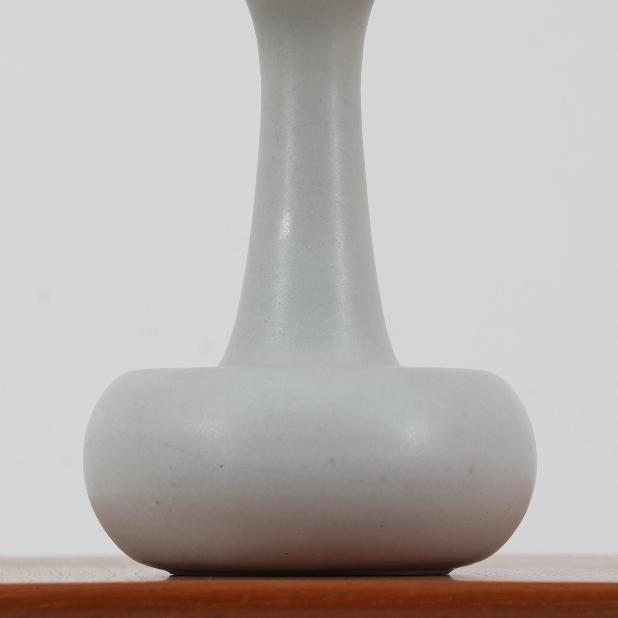 デンマークの照明ブランド Le Klint（レ・クリント）によるテーブルランプで、デザイナーは Ole Boggild（オーレ・ボギル）です。シェードは Le Klint 社製ではありませんが、新品のリネン製プリーツシェードを合わせており、全体として上品で柔らかな印象に仕上がっています。丸みを帯びた陶磁器ベースに、すらりと伸びるネックの造形が美しく、北欧デザインらしい穏やかな佇まいを感じさせます。ややグレーがかったマットな質感が上品で、リネンシェードを通した柔らかな光が空間を優しく包み込みます。シンプルながら存在感があり、リビングやベッドサイドなどさまざまなシーンでお使いいただけます。北欧の上質な灯りをお楽しみいただけるビンテージランプです。