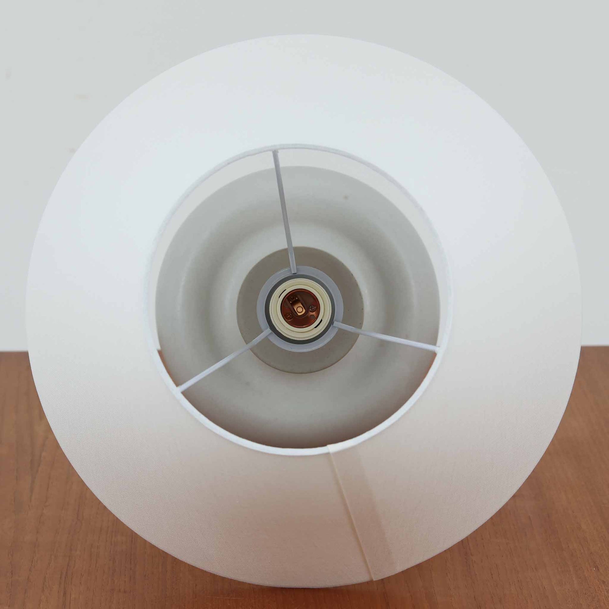 デンマークの照明ブランド Le Klint（レ・クリント）によるテーブルランプで、デザイナーは Ole Boggild（オーレ・ボギル）です。シェードは Le Klint 社製ではありませんが、新品のリネン製プリーツシェードを合わせており、全体として上品で柔らかな印象に仕上がっています。丸みを帯びた陶磁器ベースに、すらりと伸びるネックの造形が美しく、北欧デザインらしい穏やかな佇まいを感じさせます。ややグレーがかったマットな質感が上品で、リネンシェードを通した柔らかな光が空間を優しく包み込みます。シンプルながら存在感があり、リビングやベッドサイドなどさまざまなシーンでお使いいただけます。北欧の上質な灯りをお楽しみいただけるビンテージランプです。