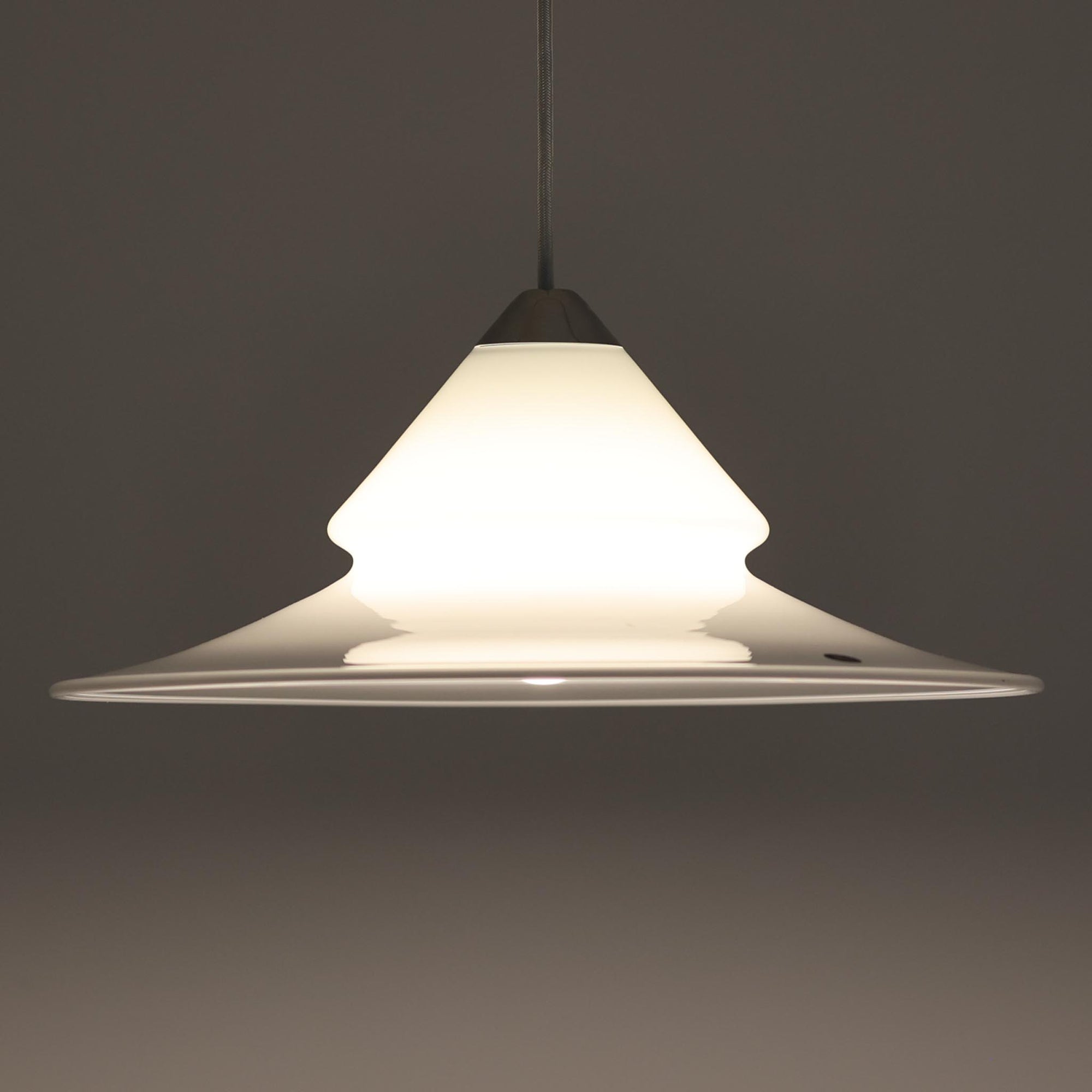 Torben Jorgensenによってデザインされ、Royal Copenhagen社から発表されたペンダントライト「Opus」です。直径42cmの大ぶりなサイズで、ガラスとアルミの組み合わせによる透明感と光沢感が際立ちます。上部のすりガラス部分から柔らかく光が広がり、下部のシェードが直接光を和らげて空間全体を心地よく照らします。シンプルでありながら優美なフォルムは、ダイニングやリビングに上質なアクセントを添え、北欧ビンテージならではのモダンで落ち着いた雰囲気を演出します。希少な一灯です。