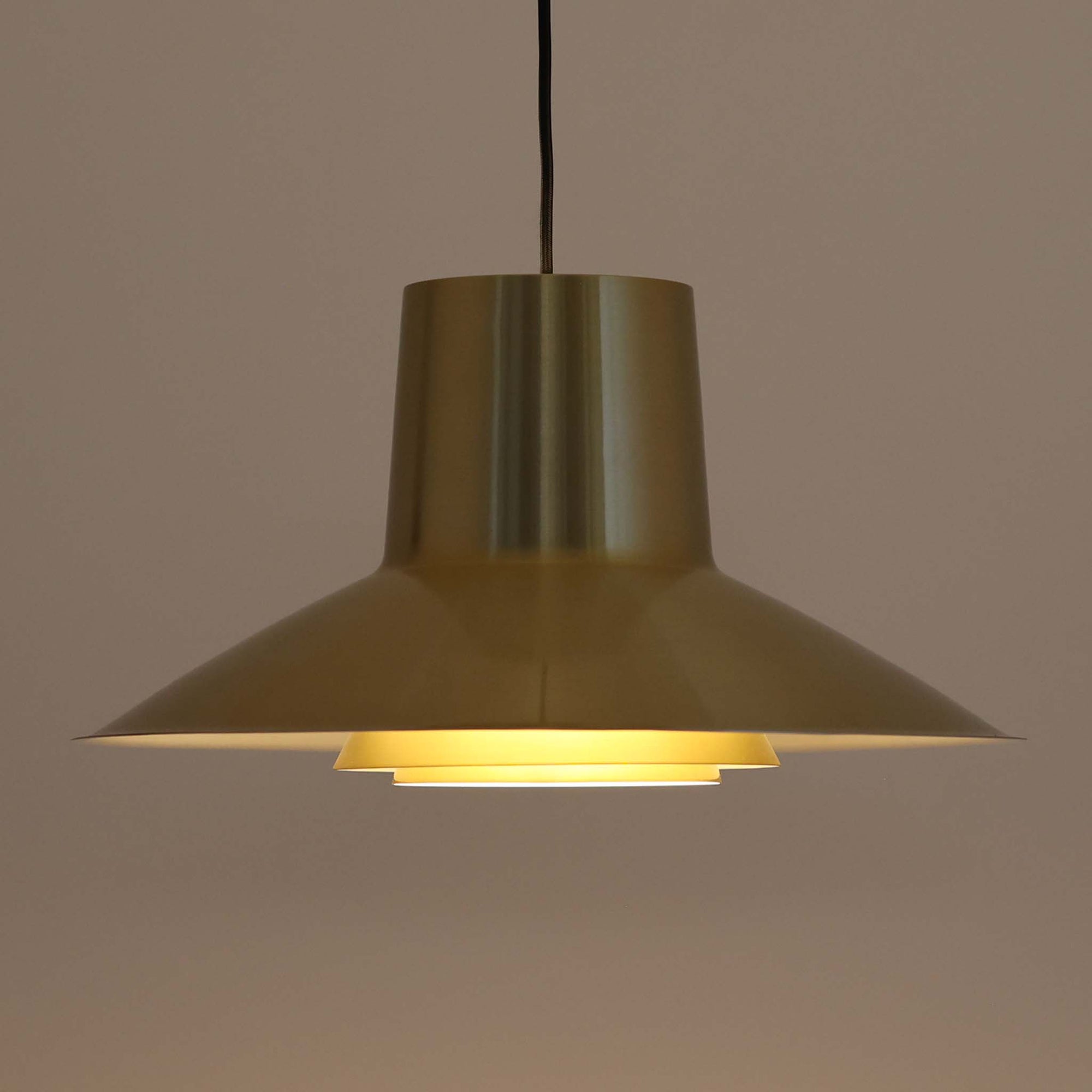 Svend Middelboeがデザインし、Nordisk Solar社より発表されたペンダントライト「Auditorie」です。直径49cmの大ぶりなサイズと、アルミ素材に施された美しい真鍮色の仕上げが特徴で、点灯時には下方向に効率よく光を届けつつ、柔らかく反射する光が空間を上品に彩ります。大胆なフォルムながらもバランスの取れたデザインは、1960年代北欧モダンのエッセンスを凝縮しており、ダイニングやリビングの主照明として存在感を放ちます。経年により深みを増した表情はビンテージならではの魅力で、機能性と美しさを兼ね備えた希少な一灯です。