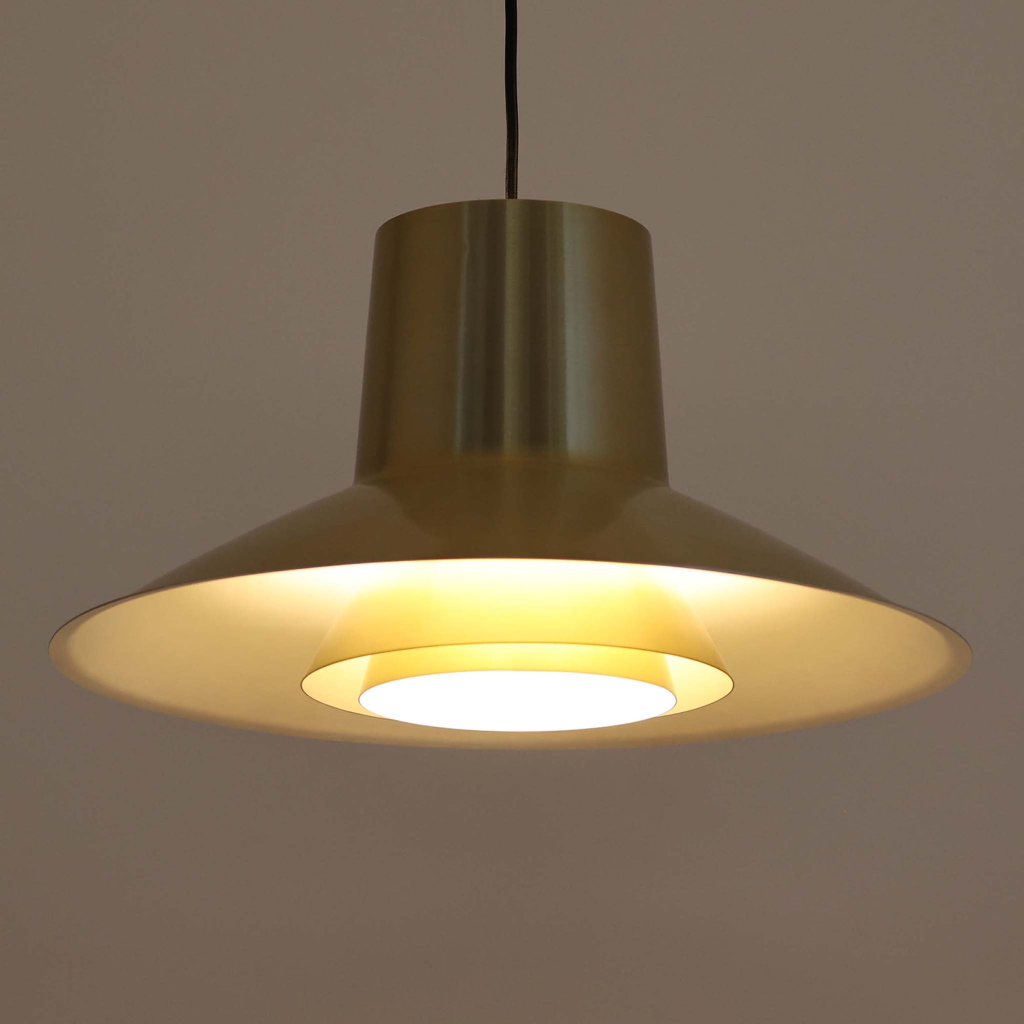 Svend Middelboeがデザインし、Nordisk Solar社より発表されたペンダントライト「Auditorie」です。直径49cmの大ぶりなサイズと、アルミ素材に施された美しい真鍮色の仕上げが特徴で、点灯時には下方向に効率よく光を届けつつ、柔らかく反射する光が空間を上品に彩ります。大胆なフォルムながらもバランスの取れたデザインは、1960年代北欧モダンのエッセンスを凝縮しており、ダイニングやリビングの主照明として存在感を放ちます。経年により深みを増した表情はビンテージならではの魅力で、機能性と美しさを兼ね備えた希少な一灯です。