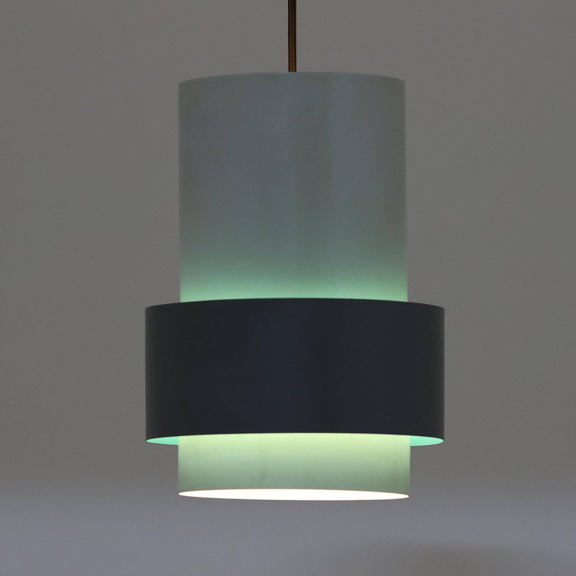 Jo HammerborgがFog & Morup社のためにデザインした「Central」ペンダントライトです。直径23cmのコンパクトなサイズながら、スチール製の二重シリンダー構造が特徴的で、点灯時には上下から光が広がり独特の陰影を演出します。外側のグレーと内側のホワイトがコントラストを生み、点灯時にはほのかなグリーンの光が漏れ出す美しいデザインです。ダイニングや小スペースに適したサイズで、北欧モダンのエッセンスを感じさせるビンテージ照明です。シェードの内側に施されたグリーンの塗装が、点灯時に柔らかなニュアンスを加え、空間に独特の雰囲気を演出します。