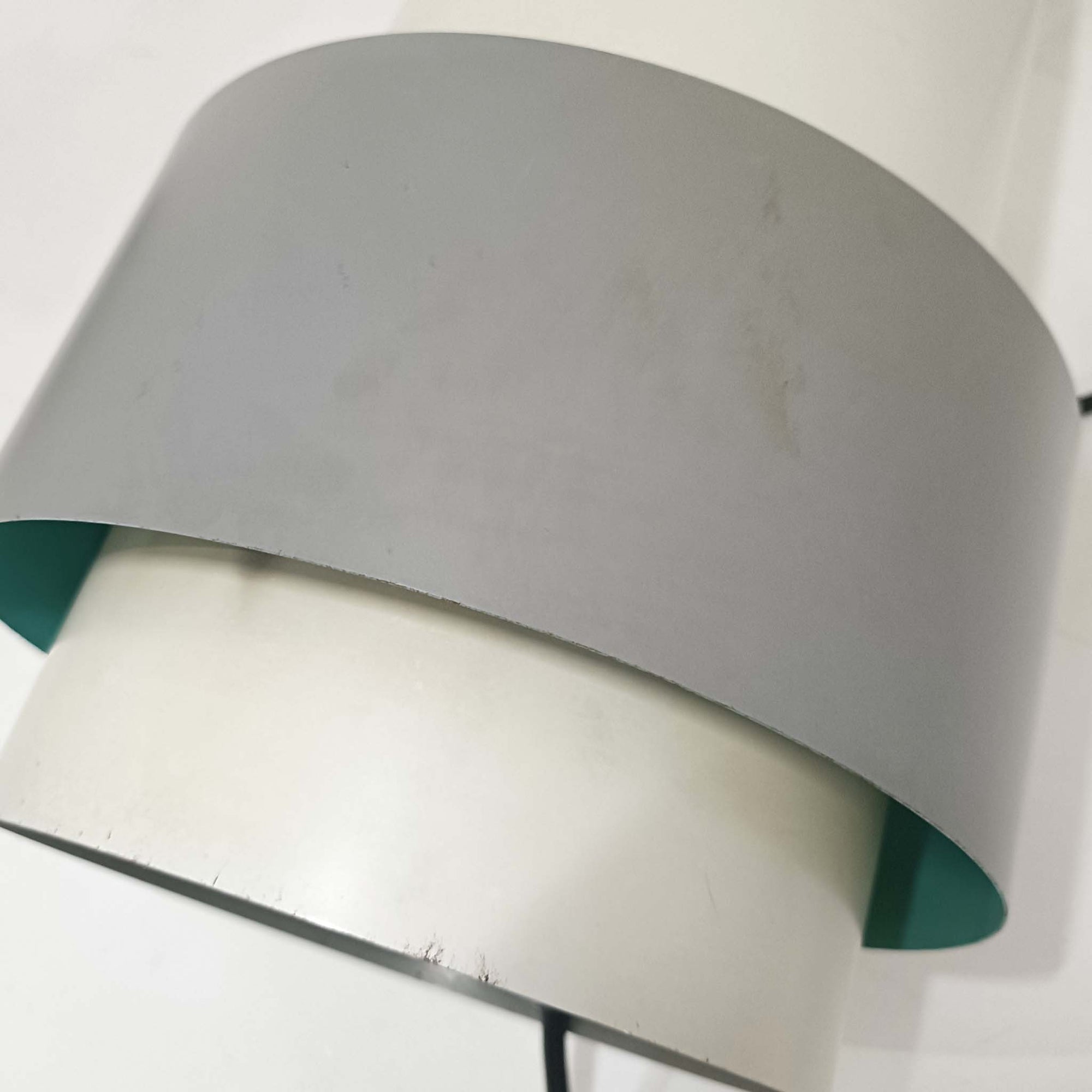 Jo HammerborgがFog &amp; Morup社のためにデザインした「Central」ペンダントライトです。直径23cmのコンパクトなサイズながら、スチール製の二重シリンダー構造が特徴的で、点灯時には上下から光が広がり独特の陰影を演出します。外側のグレーと内側のホワイトがコントラストを生み、点灯時にはほのかなグリーンの光が漏れ出す美しいデザインです。ダイニングや小スペースに適したサイズで、北欧モダンのエッセンスを感じさせるビンテージ照明です。シェードの内側に施されたグリーンの塗装が、点灯時に柔らかなニュアンスを加え、空間に独特の雰囲気を演出します。