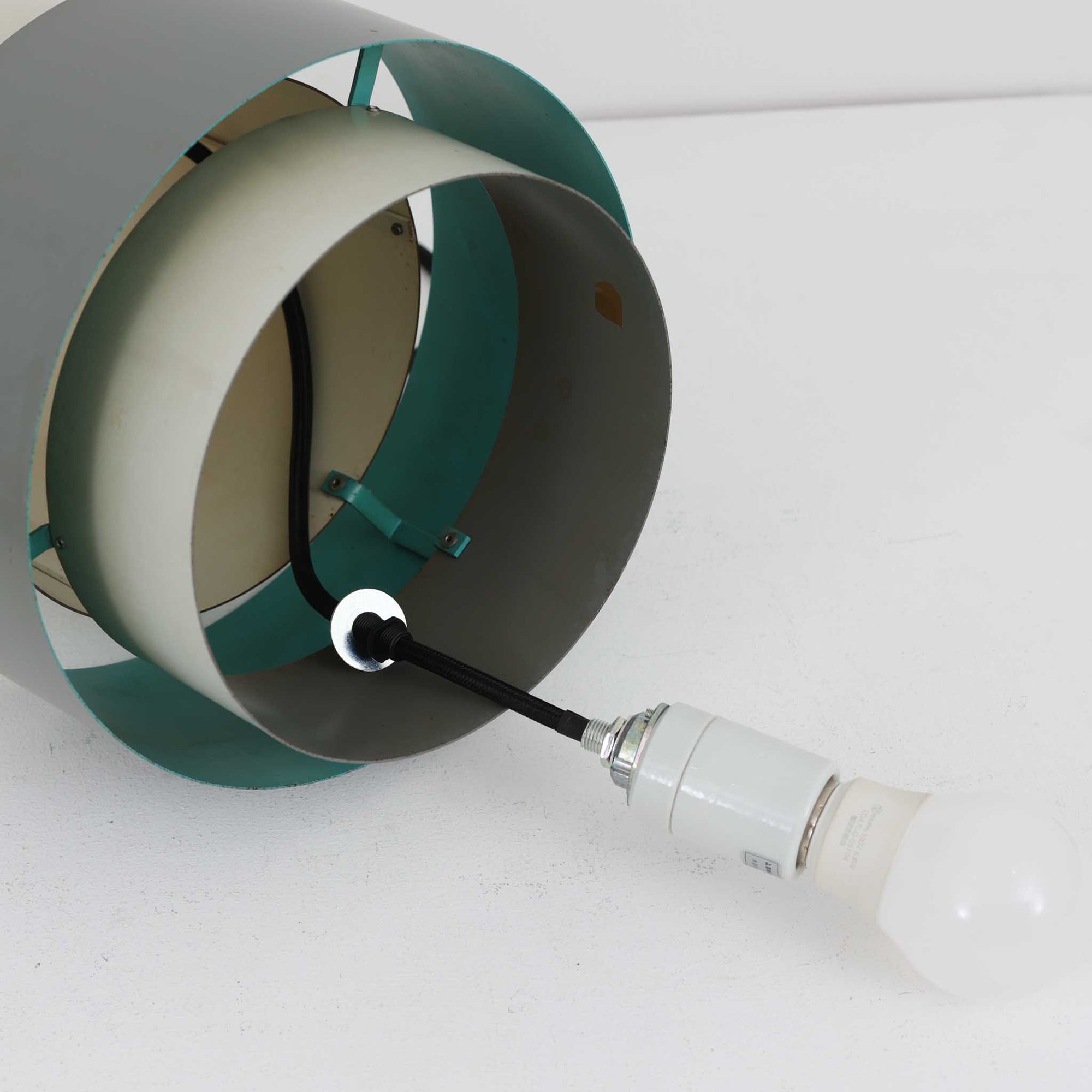 Jo HammerborgがFog &amp; Morup社のためにデザインした「Central」ペンダントライトです。直径23cmのコンパクトなサイズながら、スチール製の二重シリンダー構造が特徴的で、点灯時には上下から光が広がり独特の陰影を演出します。外側のグレーと内側のホワイトがコントラストを生み、点灯時にはほのかなグリーンの光が漏れ出す美しいデザインです。ダイニングや小スペースに適したサイズで、北欧モダンのエッセンスを感じさせるビンテージ照明です。シェードの内側に施されたグリーンの塗装が、点灯時に柔らかなニュアンスを加え、空間に独特の雰囲気を演出します。