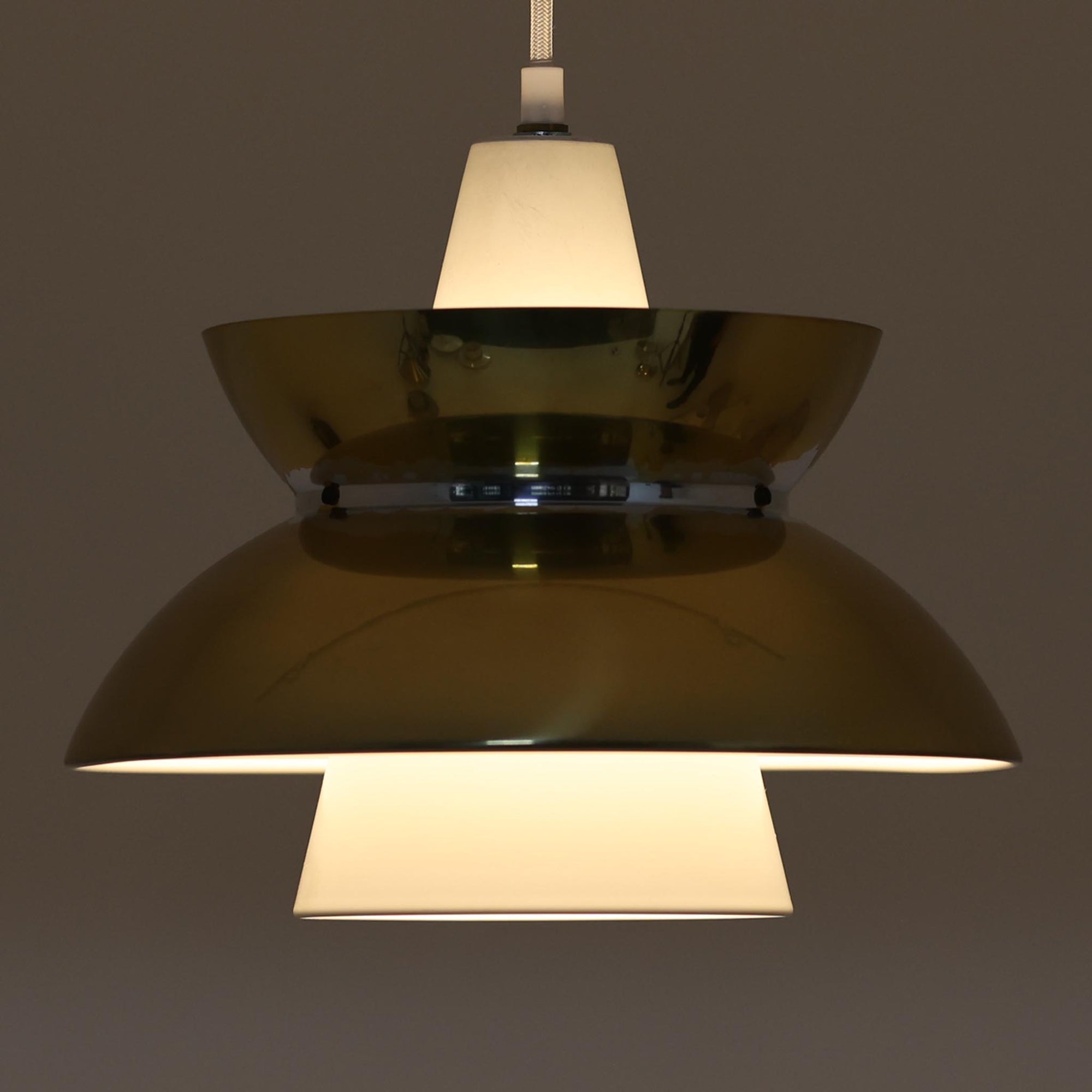 Louis Poulsen社製の小ぶりなペンダントライト「Doo-Wop」です。直径29cmの扱いやすいサイズで、真鍮カラーの上部シェードとホワイトの内側シェードのコントラストが美しいデザイン。点灯時には上下に光を広げ、空間を柔らかく照らし出します。1950年代にデンマーク海軍と共同で開発されたモデルで、シンプルながらも存在感のある佇まいが魅力です。ダイニングやキッチンに適しており、ビンテージならではの味わい深い風合いをお楽しみいただけます。さらに、現行品とは異なりシェードはマイナスネジで固定されており、当時のオリジナルならではのディテールが残されています。