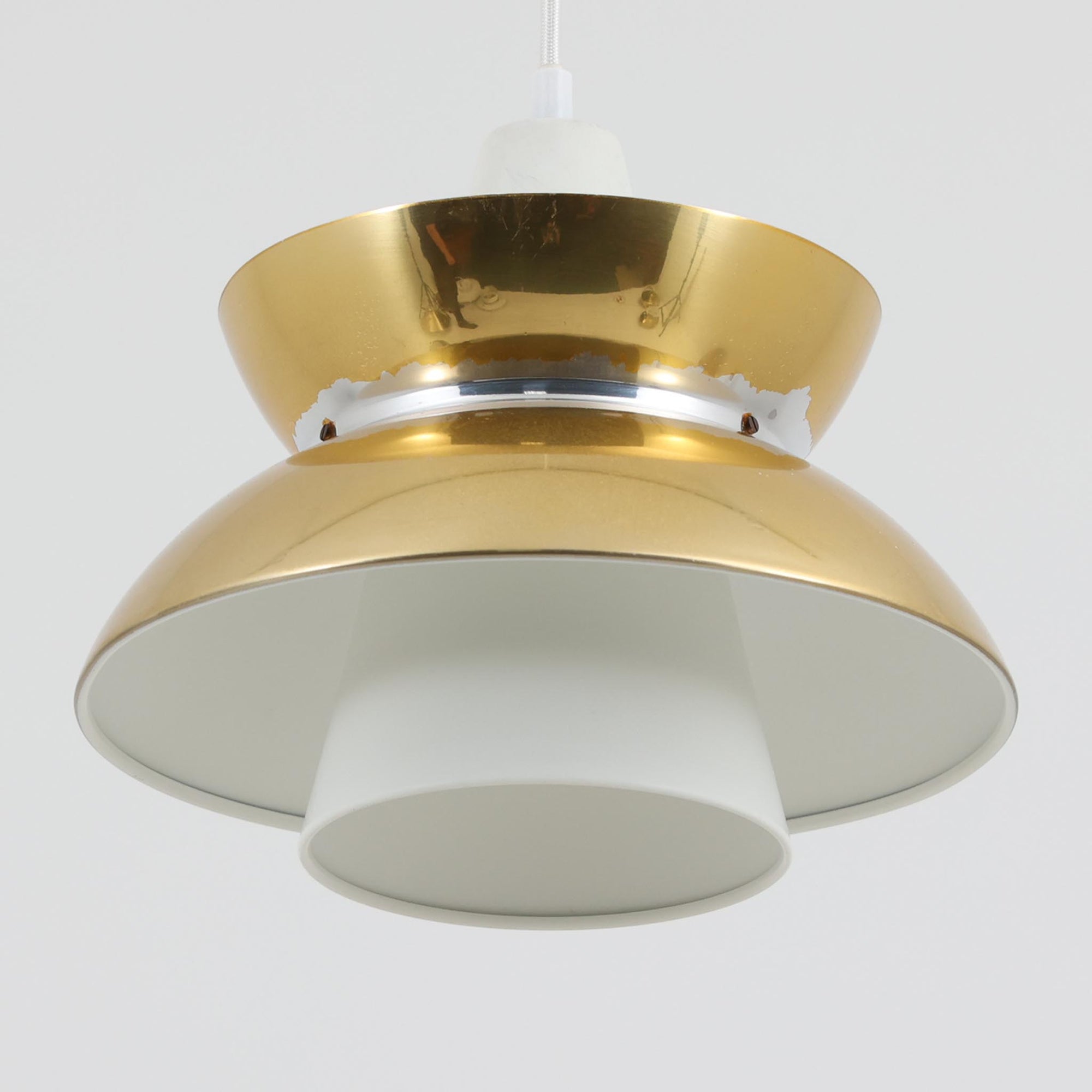 Louis Poulsen社製の小ぶりなペンダントライト「Doo-Wop」です。直径29cmの扱いやすいサイズで、真鍮カラーの上部シェードとホワイトの内側シェードのコントラストが美しいデザイン。点灯時には上下に光を広げ、空間を柔らかく照らし出します。1950年代にデンマーク海軍と共同で開発されたモデルで、シンプルながらも存在感のある佇まいが魅力です。ダイニングやキッチンに適しており、ビンテージならではの味わい深い風合いをお楽しみいただけます。さらに、現行品とは異なりシェードはマイナスネジで固定されており、当時のオリジナルならではのディテールが残されています。