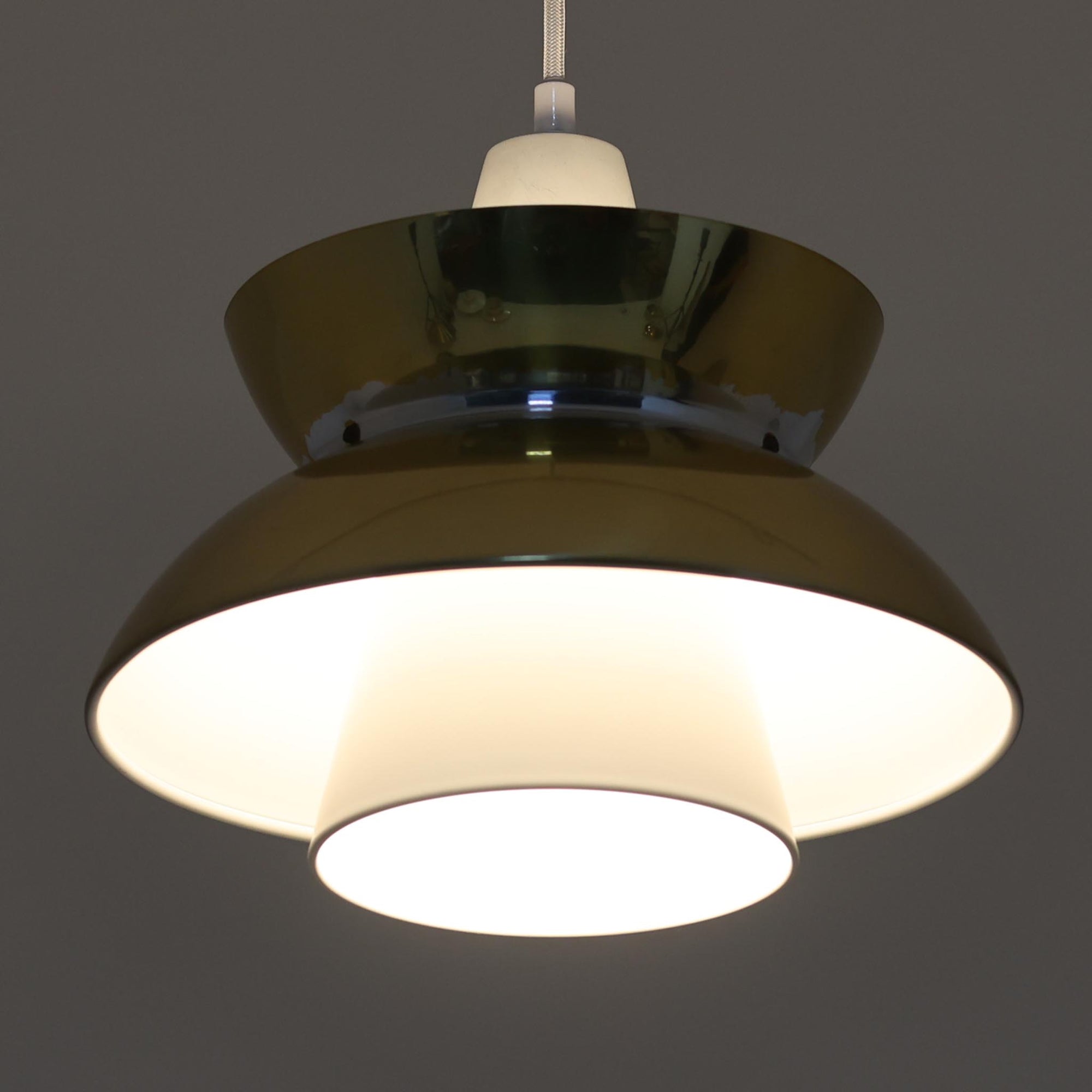 Louis Poulsen社製の小ぶりなペンダントライト「Doo-Wop」です。直径29cmの扱いやすいサイズで、真鍮カラーの上部シェードとホワイトの内側シェードのコントラストが美しいデザイン。点灯時には上下に光を広げ、空間を柔らかく照らし出します。1950年代にデンマーク海軍と共同で開発されたモデルで、シンプルながらも存在感のある佇まいが魅力です。ダイニングやキッチンに適しており、ビンテージならではの味わい深い風合いをお楽しみいただけます。さらに、現行品とは異なりシェードはマイナスネジで固定されており、当時のオリジナルならではのディテールが残されています。