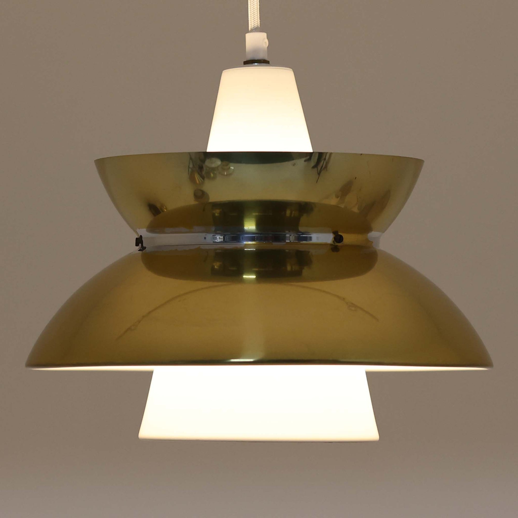 Louis Poulsen社製の小ぶりなペンダントライト「Doo-Wop」です。直径29cmの扱いやすいサイズで、真鍮カラーの上部シェードとホワイトの内側シェードのコントラストが美しいデザイン。点灯時には上下に光を広げ、空間を柔らかく照らし出します。1950年代にデンマーク海軍と共同で開発されたモデルで、シンプルながらも存在感のある佇まいが魅力です。ダイニングやキッチンに適しており、ビンテージならではの味わい深い風合いをお楽しみいただけます。さらに、現行品とは異なりシェードはマイナスネジで固定されており、当時のオリジナルならではのディテールが残されています。