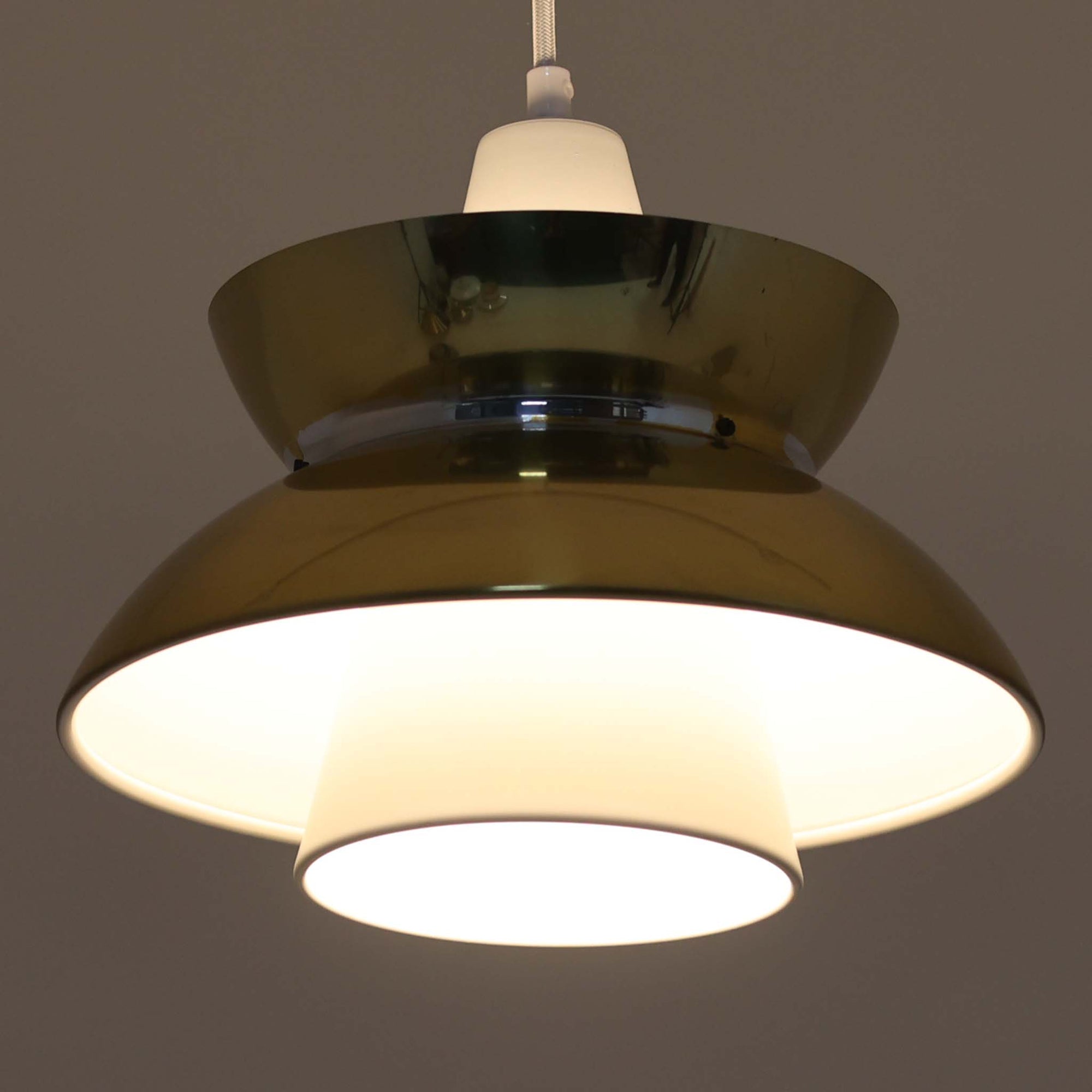 Louis Poulsen社製の小ぶりなペンダントライト「Doo-Wop」です。直径29cmの扱いやすいサイズで、真鍮カラーの上部シェードとホワイトの内側シェードのコントラストが美しいデザイン。点灯時には上下に光を広げ、空間を柔らかく照らし出します。1950年代にデンマーク海軍と共同で開発されたモデルで、シンプルながらも存在感のある佇まいが魅力です。ダイニングやキッチンに適しており、ビンテージならではの味わい深い風合いをお楽しみいただけます。さらに、現行品とは異なりシェードはマイナスネジで固定されており、当時のオリジナルならではのディテールが残されています。