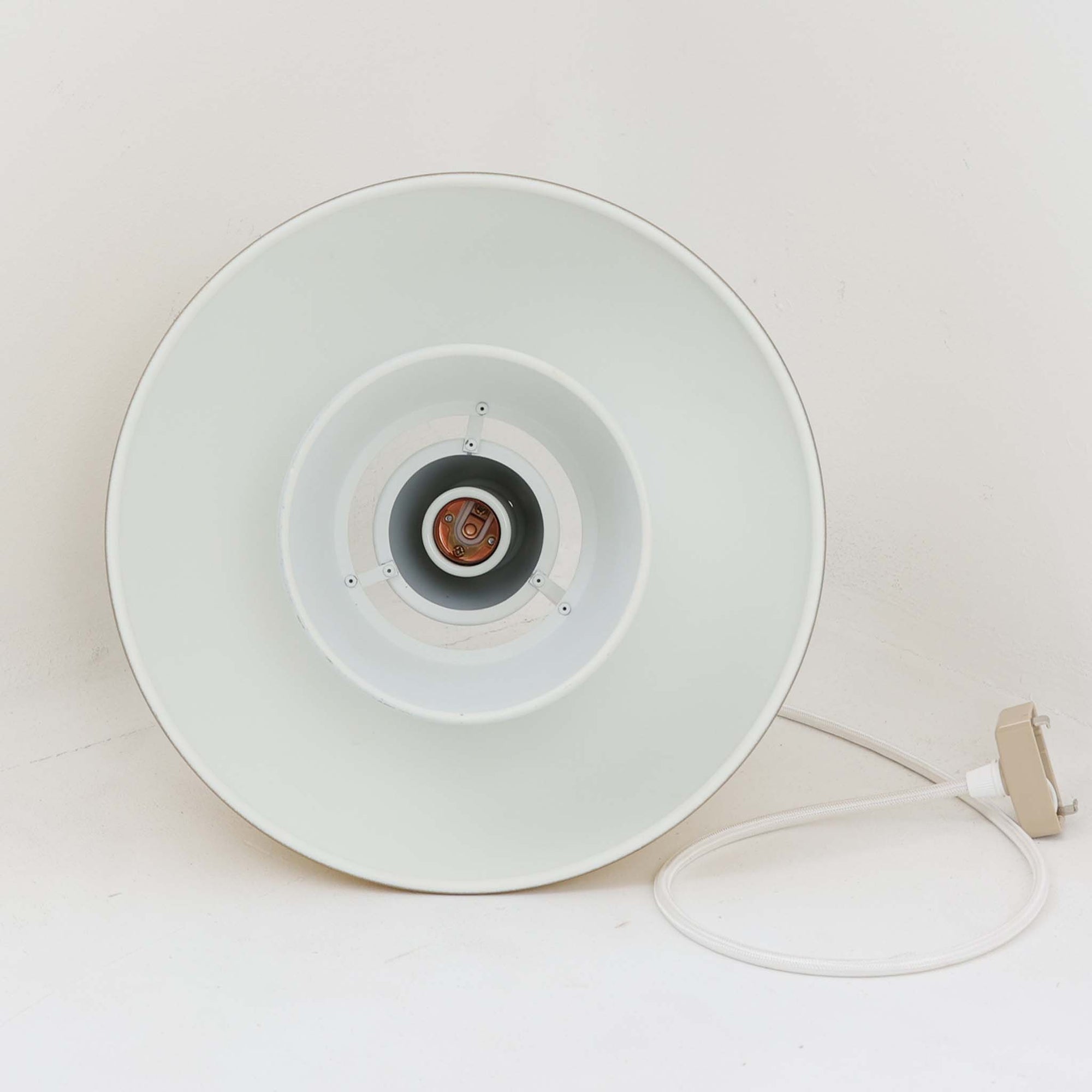 Louis Poulsen社製の小ぶりなペンダントライト「Doo-Wop」です。直径29cmの扱いやすいサイズで、真鍮カラーの上部シェードとホワイトの内側シェードのコントラストが美しいデザイン。点灯時には上下に光を広げ、空間を柔らかく照らし出します。1950年代にデンマーク海軍と共同で開発されたモデルで、シンプルながらも存在感のある佇まいが魅力です。ダイニングやキッチンに適しており、ビンテージならではの味わい深い風合いをお楽しみいただけます。さらに、現行品とは異なりシェードはマイナスネジで固定されており、当時のオリジナルならではのディテールが残されています。