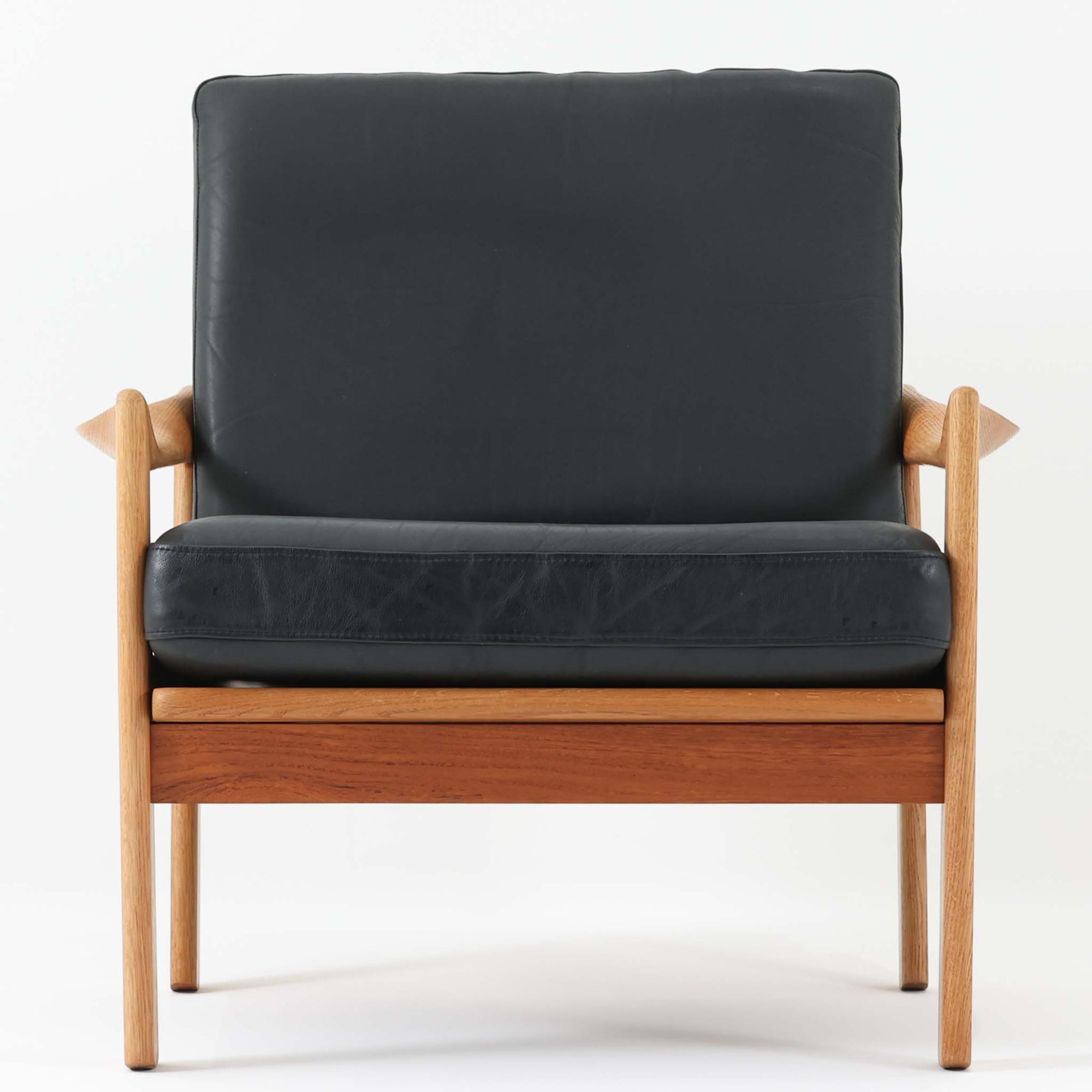 イルム・ヴィケルソーが手掛け、アイラーセン社によって製作されたシングルソファは、オーク材の堅牢なフレームとオリジナルの本革クッションを組み合わせた北欧ビンテージらしい一脚で、緩やかに削り出されたアームや直線と曲線を巧みに融合した構造が、落ち着きと彫刻的な存在感を生み出しています。座面と背もたれはしっかりとした厚みがあり、身体を包み込むような座り心地で、読書やくつろぎの時間に最適です。経年により深みを増した木肌と本革ならではの風合いが空間に上質な雰囲気をもたらし、リビングの主役としても書斎やラウンジのアクセントとしても活躍します。