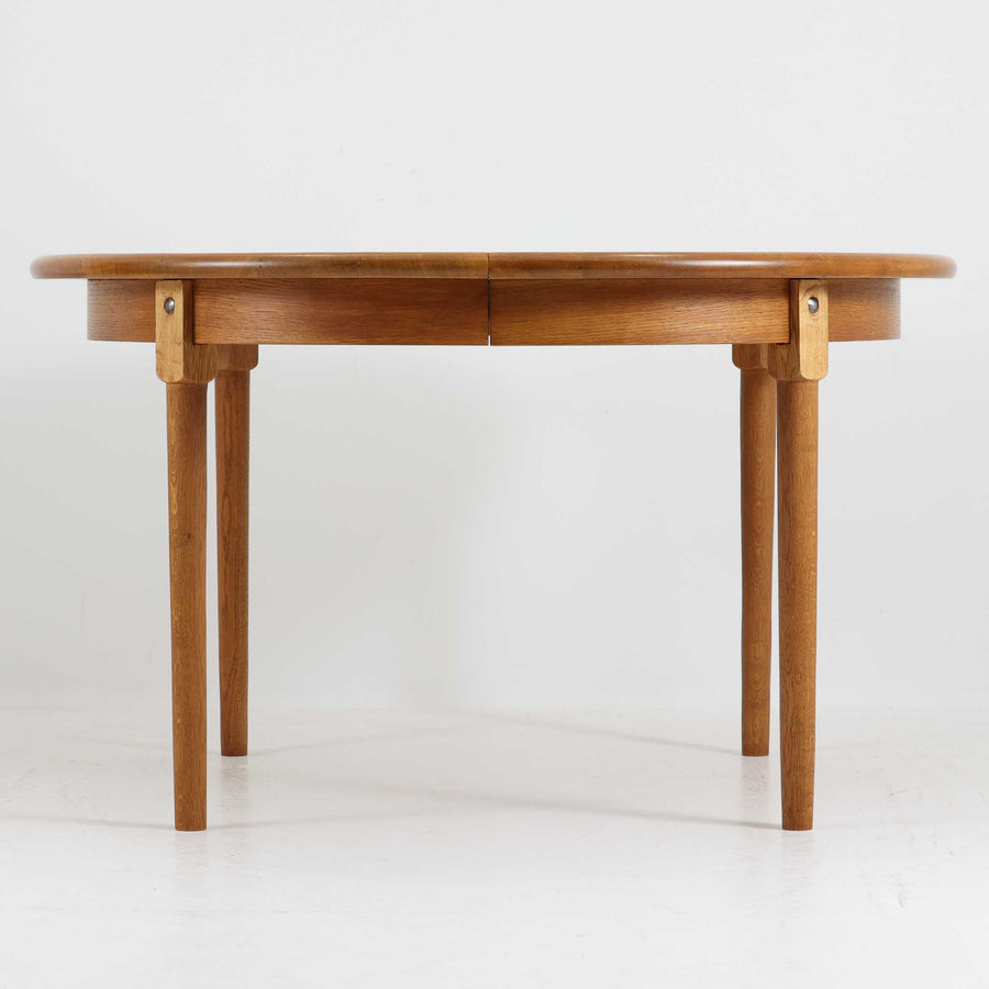 デンマーク製の円形エクステンションダイニングテーブルです。天板には贅沢にオーク無垢材が使用され、木の温もりとしっかりとした造りが魅力。拡張板にはオーク突板が用いられており、ラウンド形状からオーバル形状へと変化する機能的な構造が特徴です。経年により深みを増した木肌が味わい深く、北欧ビンテージならではの温かみのある雰囲気を演出します。普段の食卓としてはもちろん、来客時にも活躍する実用性と美しさを兼ね備えた一台です。