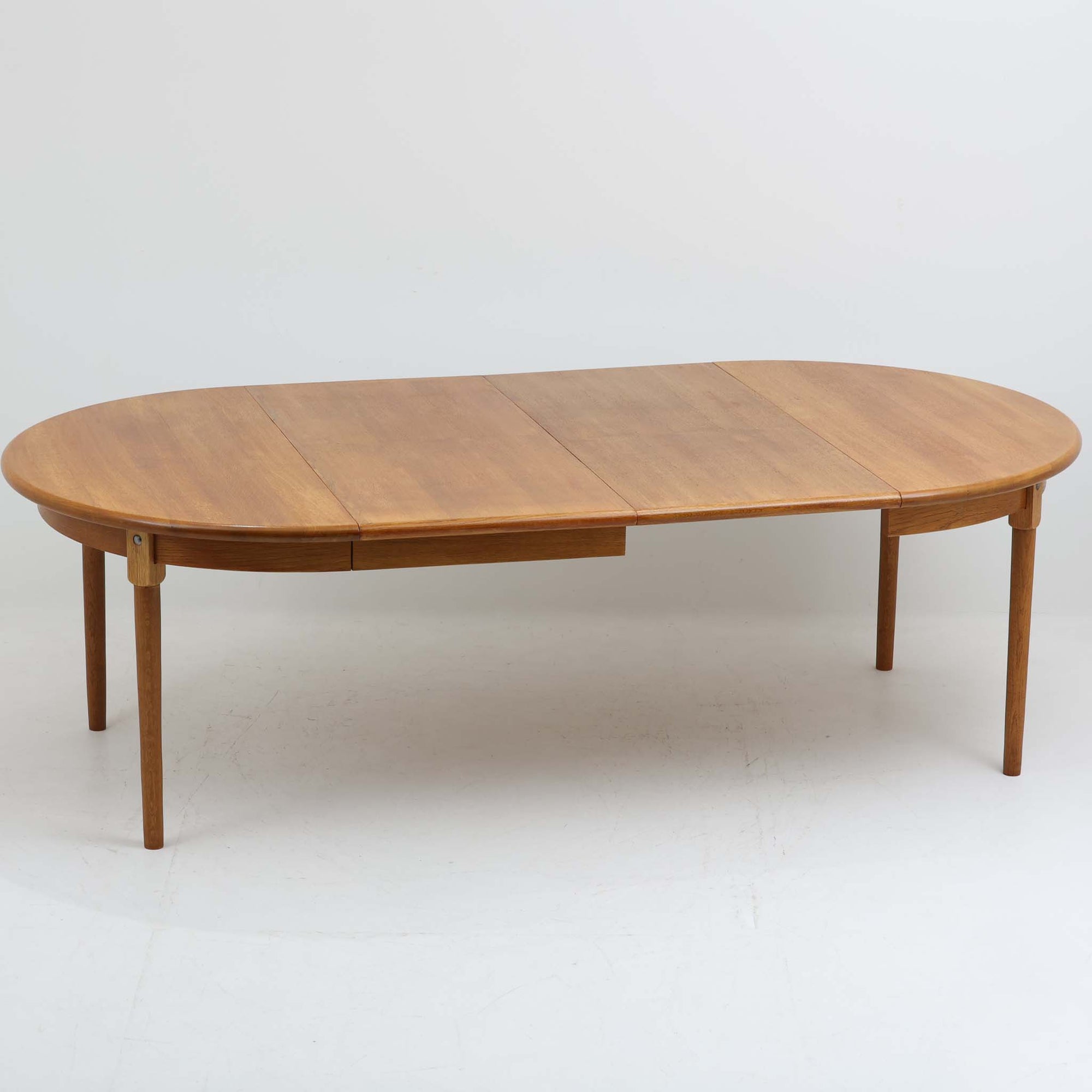 デンマーク製の円形エクステンションダイニングテーブルです。天板には贅沢にオーク無垢材が使用され、木の温もりとしっかりとした造りが魅力。拡張板にはオーク突板が用いられており、ラウンド形状からオーバル形状へと変化する機能的な構造が特徴です。経年により深みを増した木肌が味わい深く、北欧ビンテージならではの温かみのある雰囲気を演出します。普段の食卓としてはもちろん、来客時にも活躍する実用性と美しさを兼ね備えた一台です。