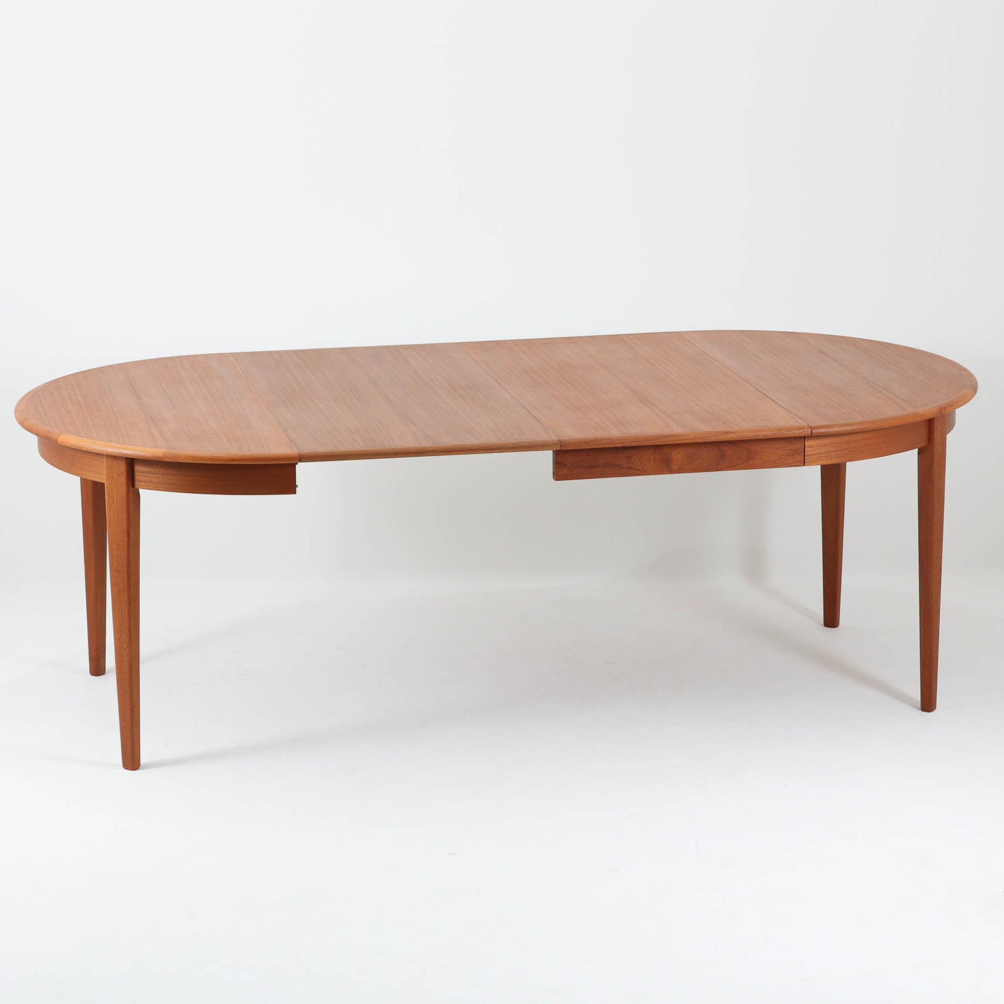 デンマーク製の北欧ビンテージ円形ダイニングテーブルです。チーク材の美しい木目が天板いっぱいに広がり、縁に施されたなだらかな丸みがやわらかな印象を与えます。幅110cmから165cm、さらに220cmまで拡張可能なエクステンション構造で、来客時にもゆとりあるレイアウトを実現。幕板から脚部へとつながる端正なフォルムは職人の確かな技術を感じさせます。家族の団らんからホームパーティーまで幅広く活躍し、経年により深みを増した色艶が空間に温もりと存在感をもたらす一台です。