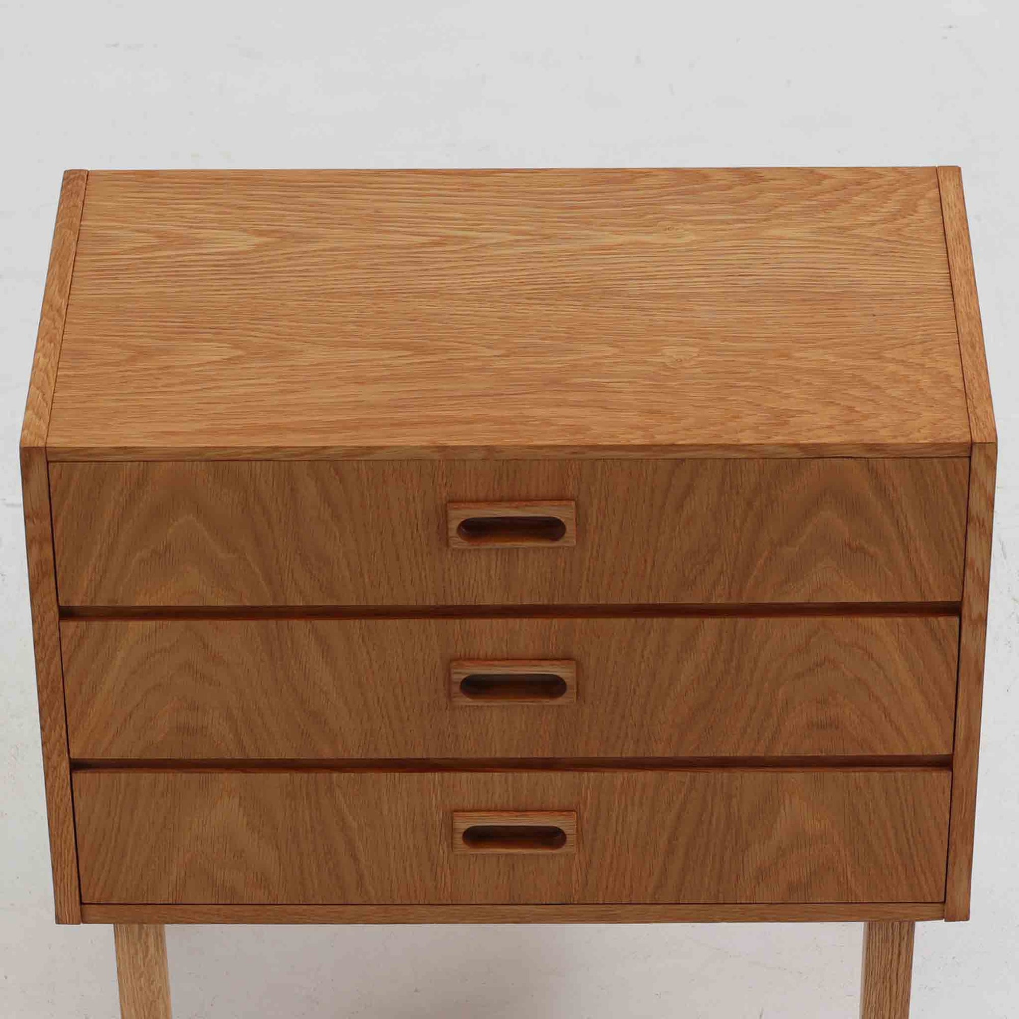 デンマーク製3段チェストです。オーク材の明るく柔らかな木目が美しく、北欧家具らしいナチュラルな温もりを感じさせます。引き出しは浅すぎず程よい深さがあり、衣類や小物をすっきりと収納できます。中央に設けられた長方形の掘り込み取っ手がすっきりとした印象を与え、シンプルなフォルムながらも職人技が光ります。小ぶりなサイズ感で、寝室や玄関、リビングのサイドチェストとしても使いやすい一台です。経年により増した風合いが空間に上質な味わいを添えます。