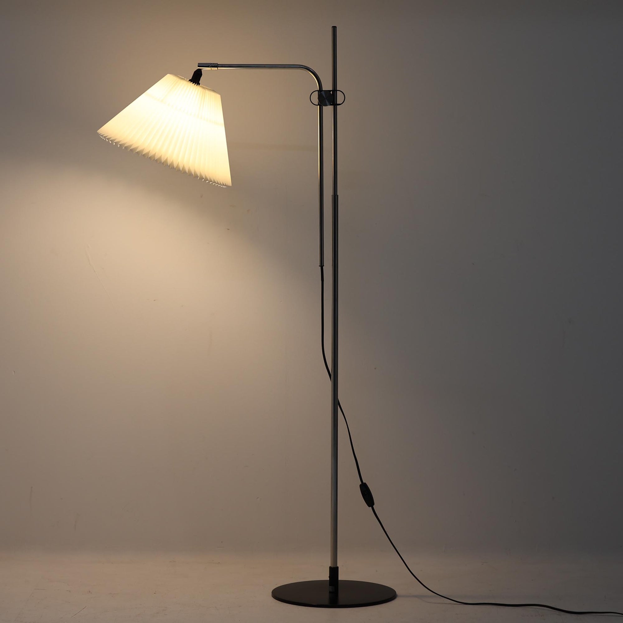 Michael Bang（マイケル・バン）によるデザインで、Le Klint（レ・クリント）から発表されたフロアランプModel 321です。高さ131cmのスチール製フレームは、無駄のない直線的なフォルムと精巧なディテールが際立ち、モダンな空間に調和します。特徴的なスライド機構によりランプの高さを調整でき、読書灯から間接照明まで幅広い用途に対応。ハンドクラフトによるプリーツシェードは柔らかい光を生み出し、北欧ビンテージならではの温もりと機能美を感じさせます。