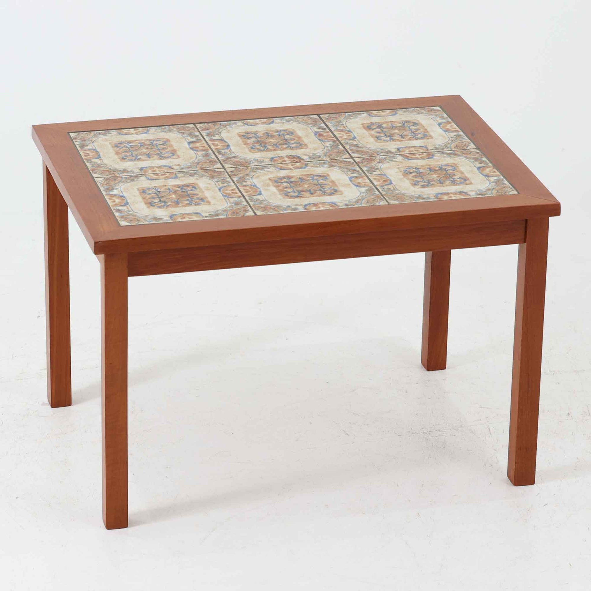 チーク材のフレームに陶磁器タイルを組み合わせたサイドテーブルは、温かみのある木肌と絵柄タイルの表情が調和した北欧ビンテージらしい一品です。天板中央に配されたタイルは、実用性に優れつつ装飾性も高く、経年による釉薬の風合いが落ち着いた存在感を演出します。直線的で端正な脚部構造は安定感があり、ソファ脇の補助台やディスプレイ台、花器やランプを置く台としても取り入れやすく、暮らしの中で静かなアクセントとなるビンテージ家具です。