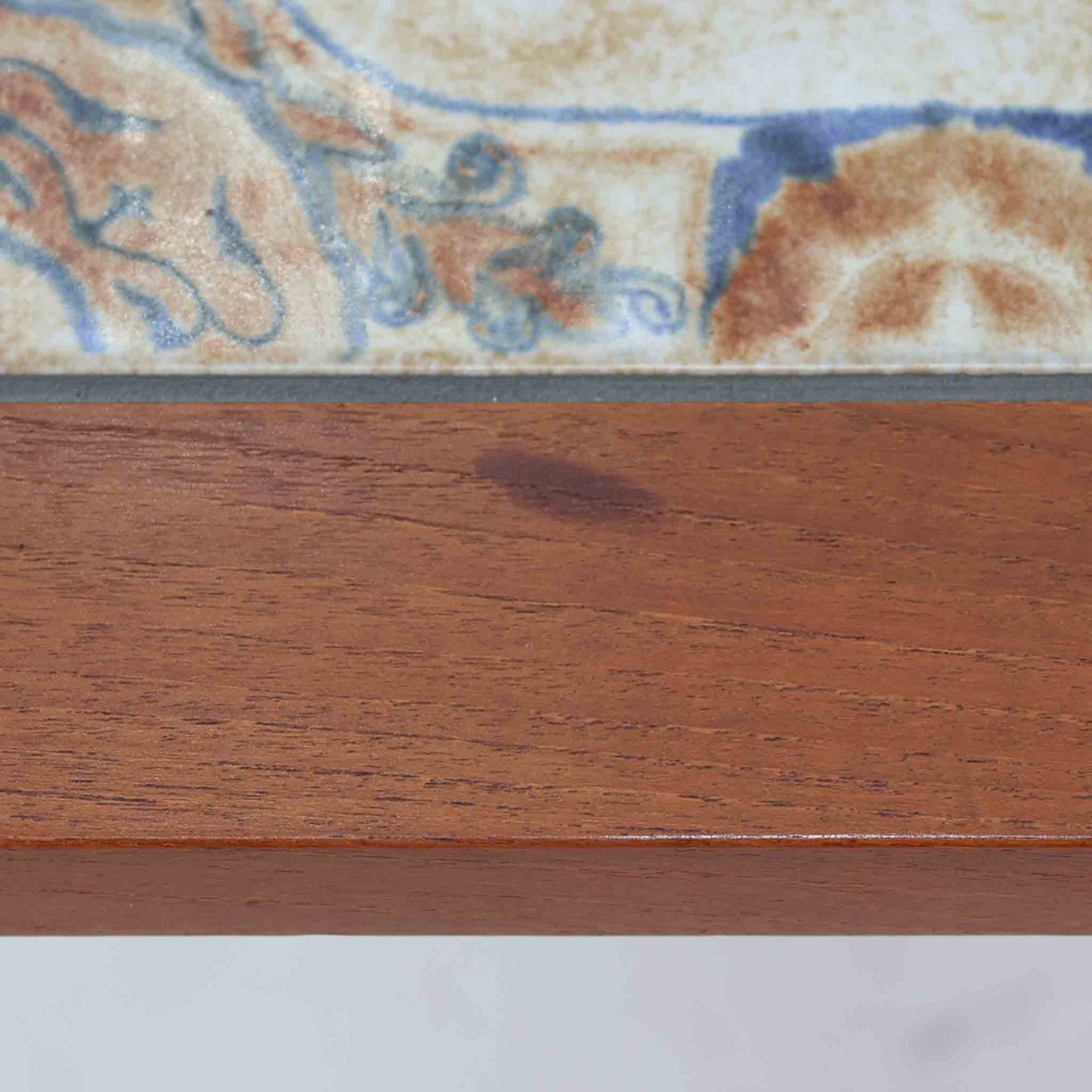 チーク材のフレームに陶磁器タイルを組み合わせたサイドテーブルは、温かみのある木肌と絵柄タイルの表情が調和した北欧ビンテージらしい一品です。天板中央に配されたタイルは、実用性に優れつつ装飾性も高く、経年による釉薬の風合いが落ち着いた存在感を演出します。直線的で端正な脚部構造は安定感があり、ソファ脇の補助台やディスプレイ台、花器やランプを置く台としても取り入れやすく、暮らしの中で静かなアクセントとなるビンテージ家具です。