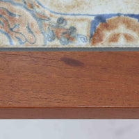 チーク材のフレームに陶磁器タイルを組み合わせたサイドテーブルは、温かみのある木肌と絵柄タイルの表情が調和した北欧ビンテージらしい一品です。天板中央に配されたタイルは、実用性に優れつつ装飾性も高く、経年による釉薬の風合いが落ち着いた存在感を演出します。直線的で端正な脚部構造は安定感があり、ソファ脇の補助台やディスプレイ台、花器やランプを置く台としても取り入れやすく、暮らしの中で静かなアクセントとなるビンテージ家具です。