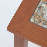 チーク材のフレームに陶磁器タイルを組み合わせたサイドテーブルは、温かみのある木肌と絵柄タイルの表情が調和した北欧ビンテージらしい一品です。天板中央に配されたタイルは、実用性に優れつつ装飾性も高く、経年による釉薬の風合いが落ち着いた存在感を演出します。直線的で端正な脚部構造は安定感があり、ソファ脇の補助台やディスプレイ台、花器やランプを置く台としても取り入れやすく、暮らしの中で静かなアクセントとなるビンテージ家具です。