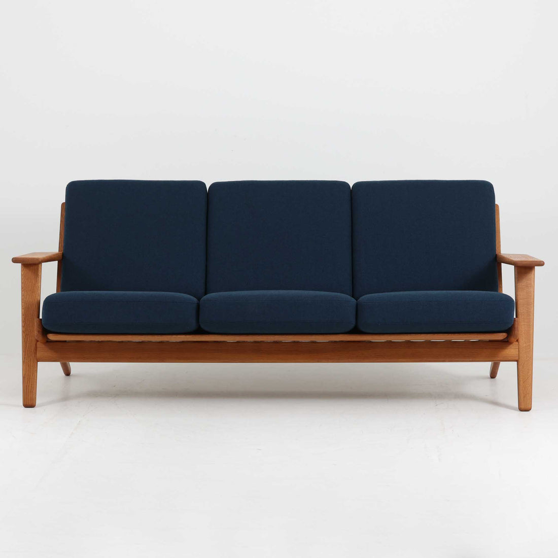 Hans J. Wegner（ハンス・J・ウェグナー）によるデザインで、Getama社から発表されたトリプルソファ「GE290」です。堅牢なオーク材フレームにボリュームのあるクッションを組み合わせた構造で、しっかりとした座り心地と安定感を実現しています。ビンテージならではのクッション内部にはスプリングが内包されており、しなやかな弾力と快適な座り心地を長く保ちます。特徴的なアームのラインや背面の格子フレームは、どの角度から見ても美しく、空間の主役となる存在感を放ちます。ブルー系ファブリックがオーク材の温もりと調和し、北欧らしい落ち着いた雰囲気を演出する名作ビンテージソファです。