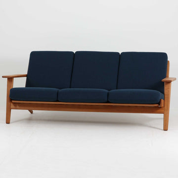 Hans J. Wegner（ハンス・J・ウェグナー）によるデザインで、Getama社から発表されたトリプルソファ「GE290」です。堅牢なオーク材フレームにボリュームのあるクッションを組み合わせた構造で、しっかりとした座り心地と安定感を実現しています。ビンテージならではのクッション内部にはスプリングが内包されており、しなやかな弾力と快適な座り心地を長く保ちます。特徴的なアームのラインや背面の格子フレームは、どの角度から見ても美しく、空間の主役となる存在感を放ちます。ブルー系ファブリックがオーク材の温もりと調和し、北欧らしい落ち着いた雰囲気を演出する名作ビンテージソファです。