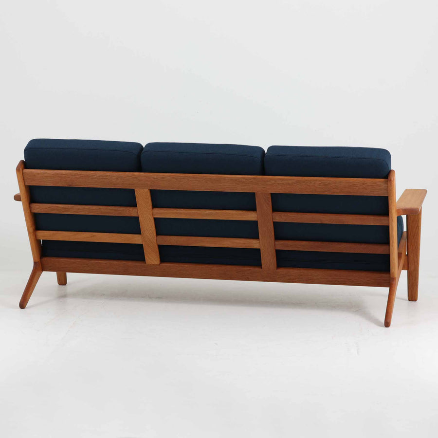 Hans J. Wegner（ハンス・J・ウェグナー）によるデザインで、Getama社から発表されたトリプルソファ「GE290」です。堅牢なオーク材フレームにボリュームのあるクッションを組み合わせた構造で、しっかりとした座り心地と安定感を実現しています。ビンテージならではのクッション内部にはスプリングが内包されており、しなやかな弾力と快適な座り心地を長く保ちます。特徴的なアームのラインや背面の格子フレームは、どの角度から見ても美しく、空間の主役となる存在感を放ちます。ブルー系ファブリックがオーク材の温もりと調和し、北欧らしい落ち着いた雰囲気を演出する名作ビンテージソファです。