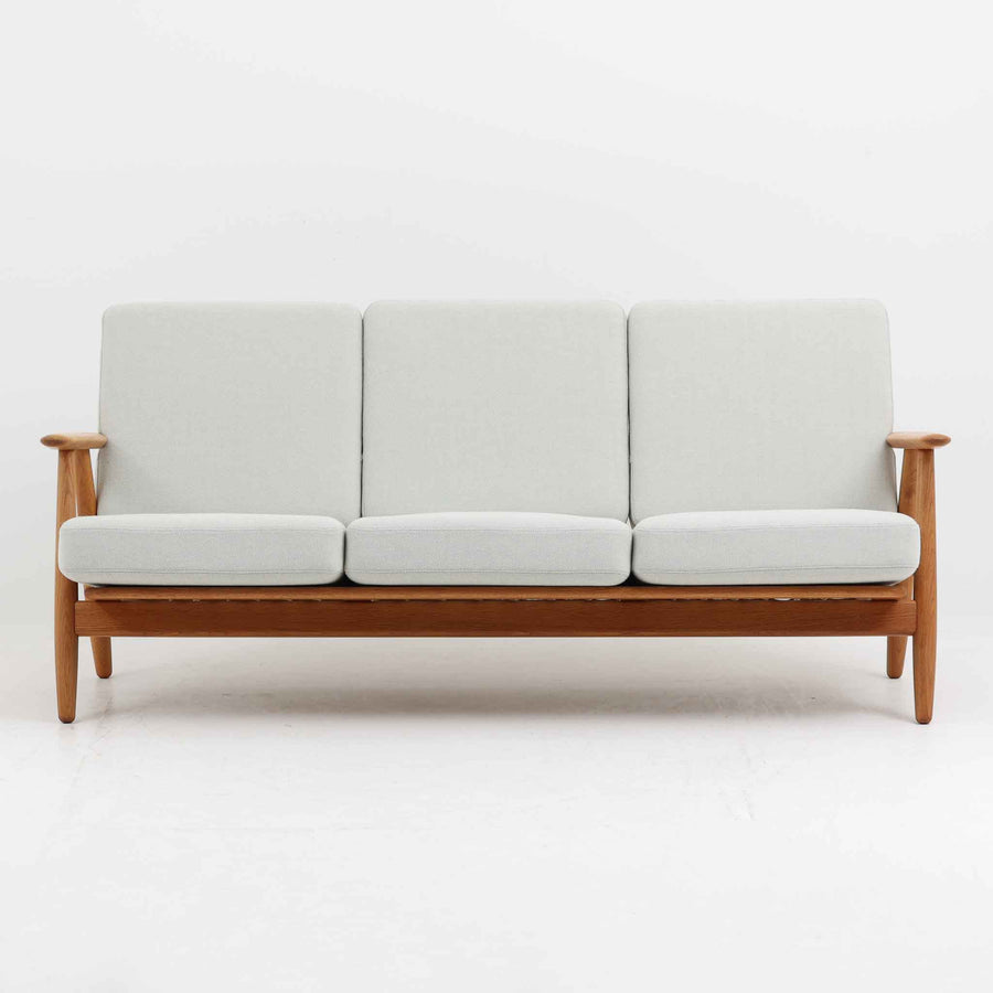 Hans J. Wegner（ハンス・J・ウェグナー）がデザインし、Getama社から発表されたGE240トリプルソファです。通称「Cigar Sofa」とも呼ばれる名作で、丸みを帯びたアームと堅牢なオーク材フレームが特徴です。背面まで美しい格子状のデザインは空間に軽やかさを与え、どの角度から見ても存在感があります。ライトグレー系の張地はアクリルとウールをブレンドした素材で、柔らかな風合いと高い耐久性を備えています。北欧家具らしいシンプルさと快適さを兼ね備え、リビングを上質に彩るビンテージソファです。