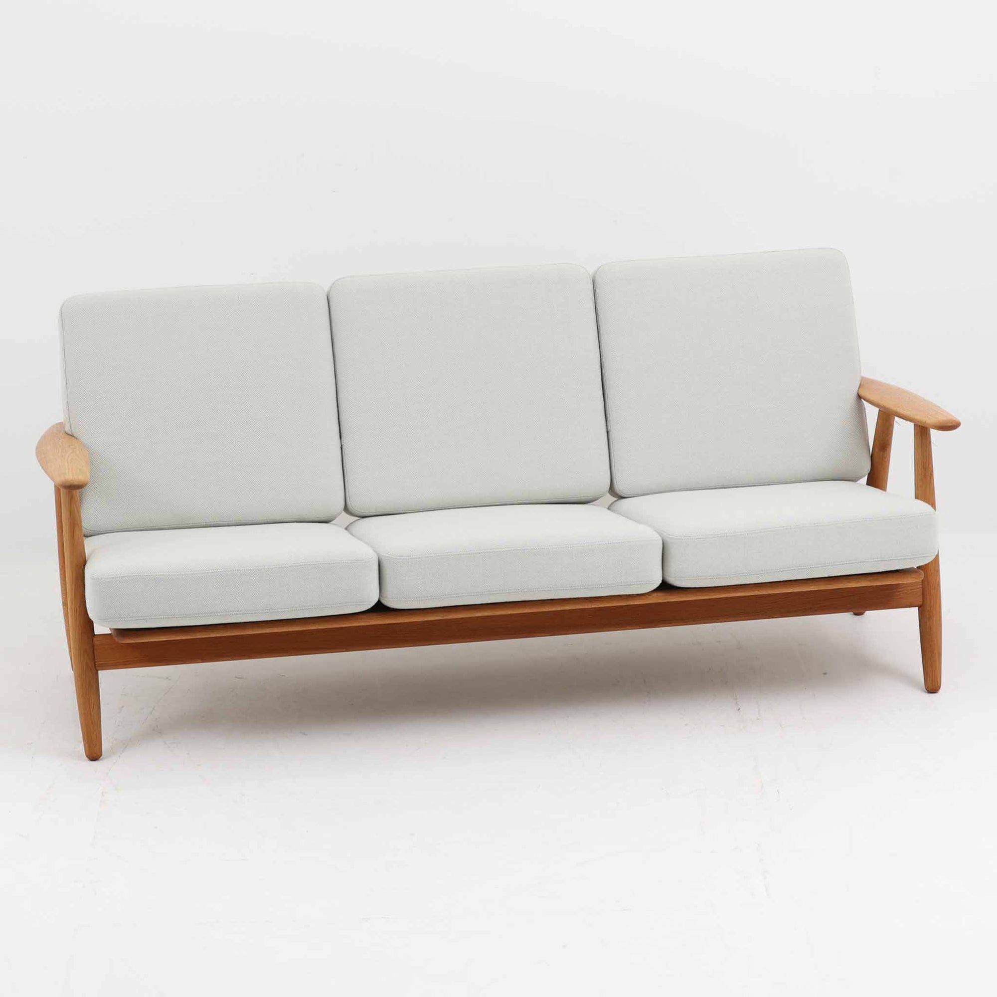 Hans J. Wegner（ハンス・J・ウェグナー）がデザインし、Getama社から発表されたGE240トリプルソファです。通称「Cigar Sofa」とも呼ばれる名作で、丸みを帯びたアームと堅牢なオーク材フレームが特徴です。背面まで美しい格子状のデザインは空間に軽やかさを与え、どの角度から見ても存在感があります。ライトグレー系の張地はアクリルとウールをブレンドした素材で、柔らかな風合いと高い耐久性を備えています。北欧家具らしいシンプルさと快適さを兼ね備え、リビングを上質に彩るビンテージソファです。