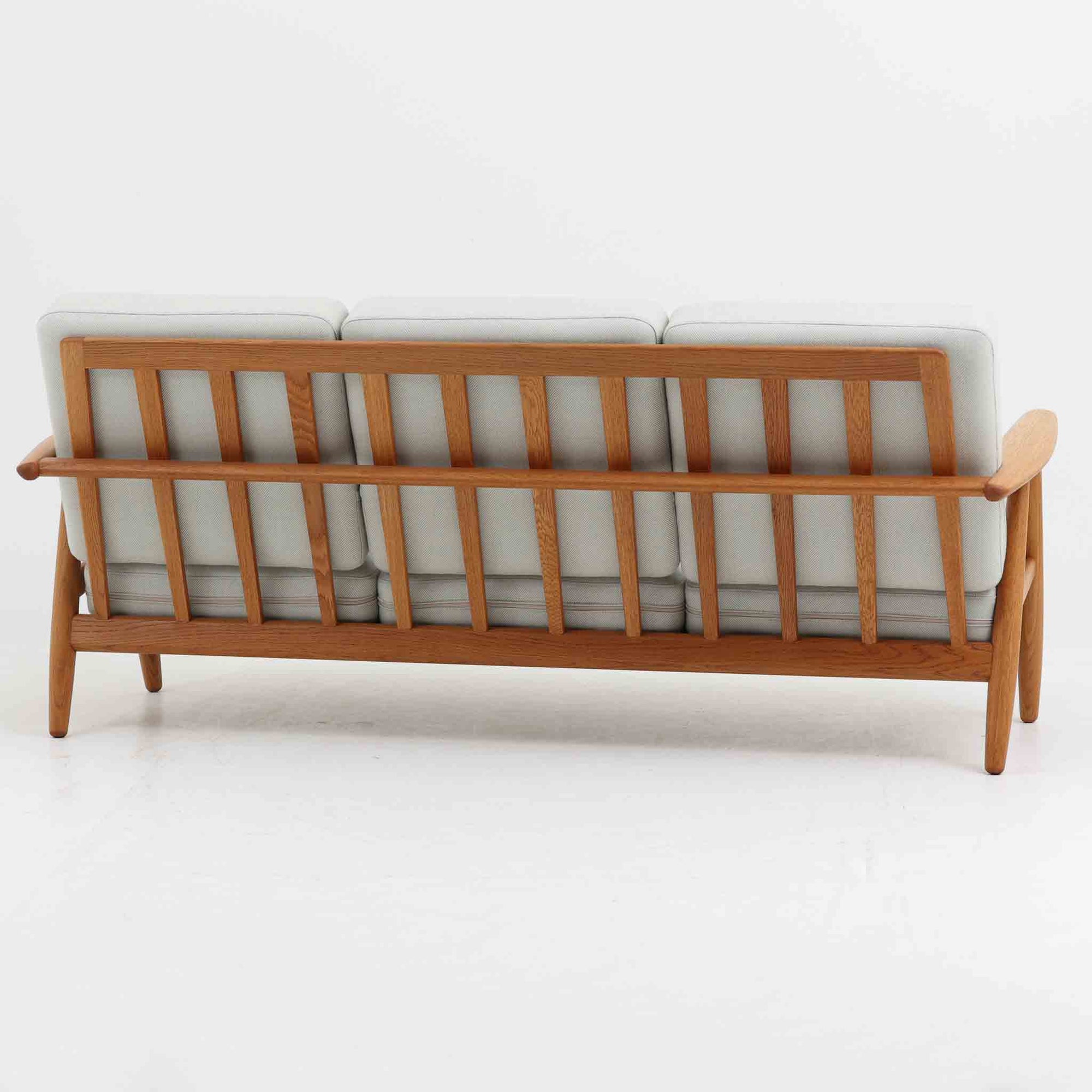 Hans J. Wegner（ハンス・J・ウェグナー）がデザインし、Getama社から発表されたGE240トリプルソファです。通称「Cigar Sofa」とも呼ばれる名作で、丸みを帯びたアームと堅牢なオーク材フレームが特徴です。背面まで美しい格子状のデザインは空間に軽やかさを与え、どの角度から見ても存在感があります。ライトグレー系の張地はアクリルとウールをブレンドした素材で、柔らかな風合いと高い耐久性を備えています。北欧家具らしいシンプルさと快適さを兼ね備え、リビングを上質に彩るビンテージソファです。