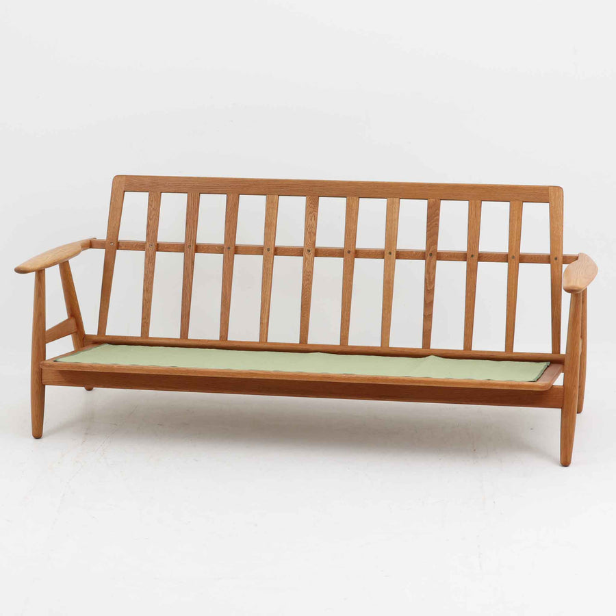 Hans J. Wegner（ハンス・J・ウェグナー）がデザインし、Getama社から発表されたGE240トリプルソファです。通称「Cigar Sofa」とも呼ばれる名作で、丸みを帯びたアームと堅牢なオーク材フレームが特徴です。背面まで美しい格子状のデザインは空間に軽やかさを与え、どの角度から見ても存在感があります。ライトグレー系の張地はアクリルとウールをブレンドした素材で、柔らかな風合いと高い耐久性を備えています。北欧家具らしいシンプルさと快適さを兼ね備え、リビングを上質に彩るビンテージソファです。