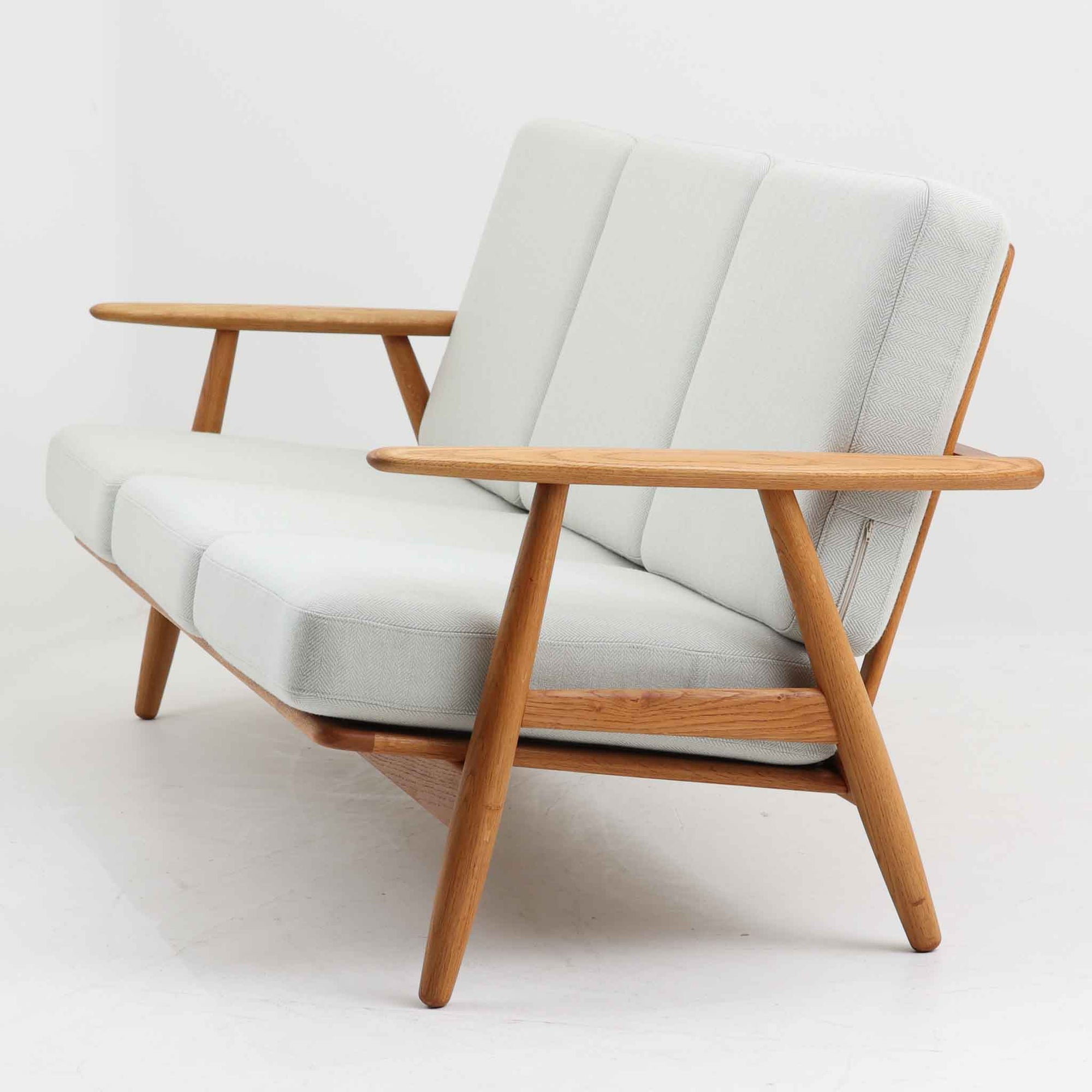 Hans J. Wegner（ハンス・J・ウェグナー）がデザインし、Getama社から発表されたGE240トリプルソファです。通称「Cigar Sofa」とも呼ばれる名作で、丸みを帯びたアームと堅牢なオーク材フレームが特徴です。背面まで美しい格子状のデザインは空間に軽やかさを与え、どの角度から見ても存在感があります。ライトグレー系の張地はアクリルとウールをブレンドした素材で、柔らかな風合いと高い耐久性を備えています。北欧家具らしいシンプルさと快適さを兼ね備え、リビングを上質に彩るビンテージソファです。