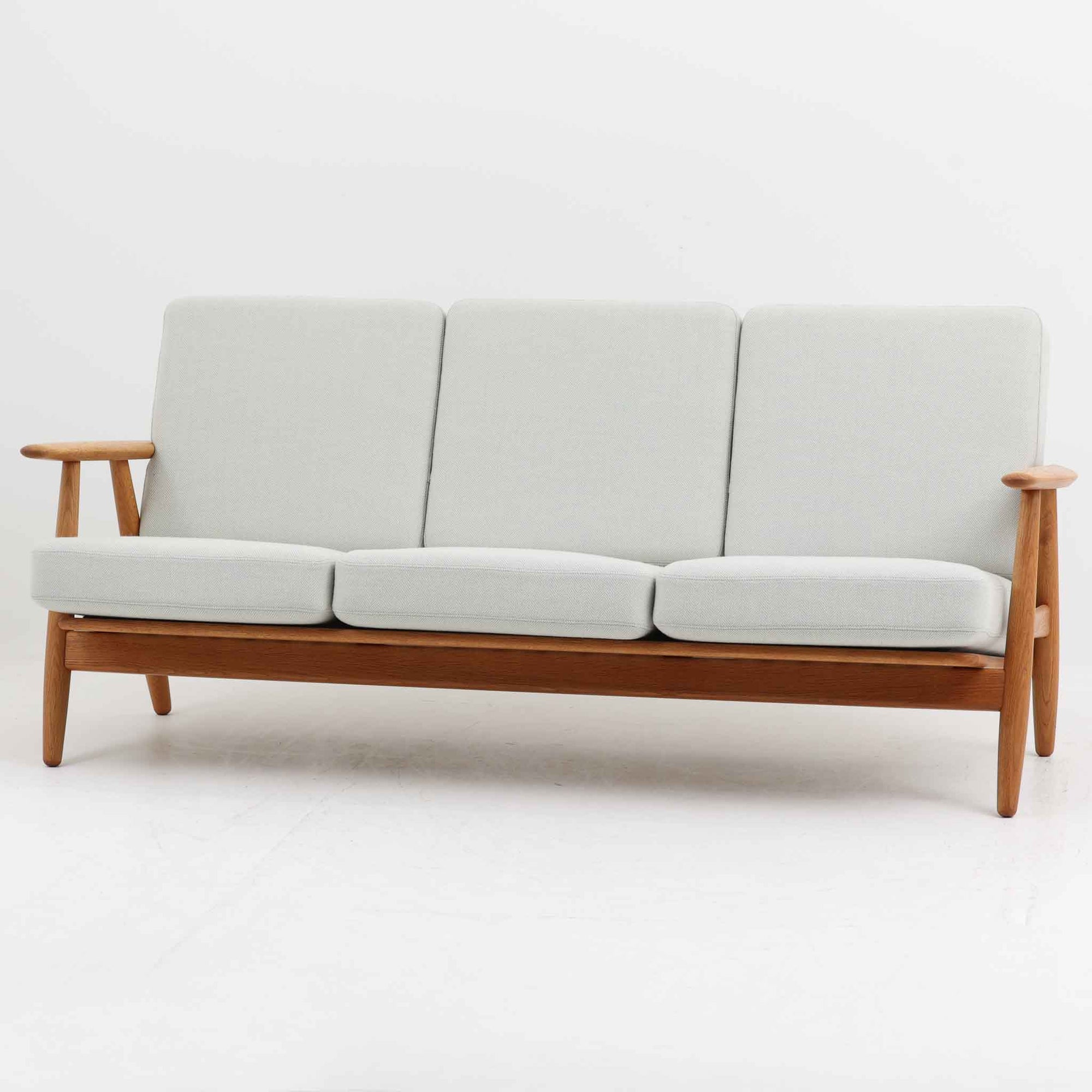 Hans J. Wegner（ハンス・J・ウェグナー）がデザインし、Getama社から発表されたGE240トリプルソファです。通称「Cigar Sofa」とも呼ばれる名作で、丸みを帯びたアームと堅牢なオーク材フレームが特徴です。背面まで美しい格子状のデザインは空間に軽やかさを与え、どの角度から見ても存在感があります。ライトグレー系の張地はアクリルとウールをブレンドした素材で、柔らかな風合いと高い耐久性を備えています。北欧家具らしいシンプルさと快適さを兼ね備え、リビングを上質に彩るビンテージソファです。