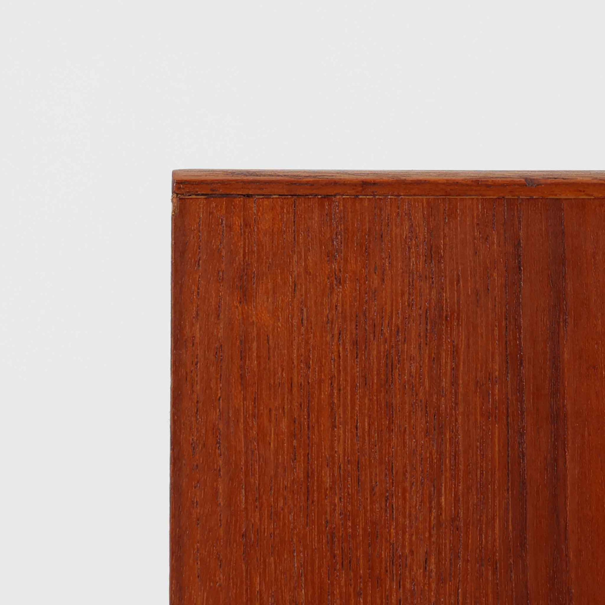 チーク材の豊かな木目が美しいこちらのサイドチェストは、北欧ビンテージらしい端正なデザインと実用性を兼ね備えた一台です。天板の縁には立ち上がりが施され、小物の転落を防ぐ工夫がされています。引き出し下のオープンスペースは本や雑貨の収納に便利で、ソファやベッドサイドに置けばサイドテーブルとしても活躍します。丸みを帯びた持ち手やテーパードレッグが柔らかな印象を与え、経年変化による木肌の深みが空間に温もりを添える逸品です。